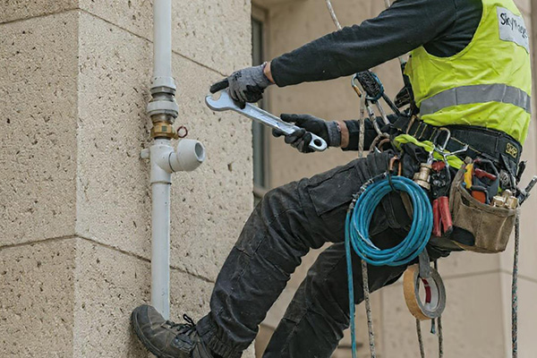 A plumber working on pipes on the side of a tall building.