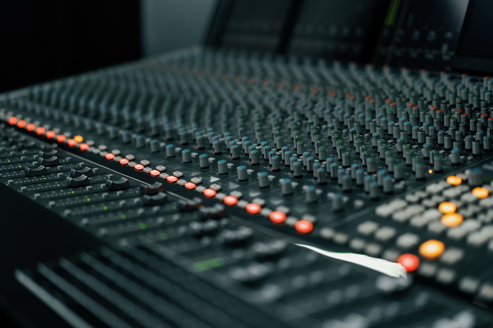 Close-up of a recording studio mixing console with faders and knobs in soft focus