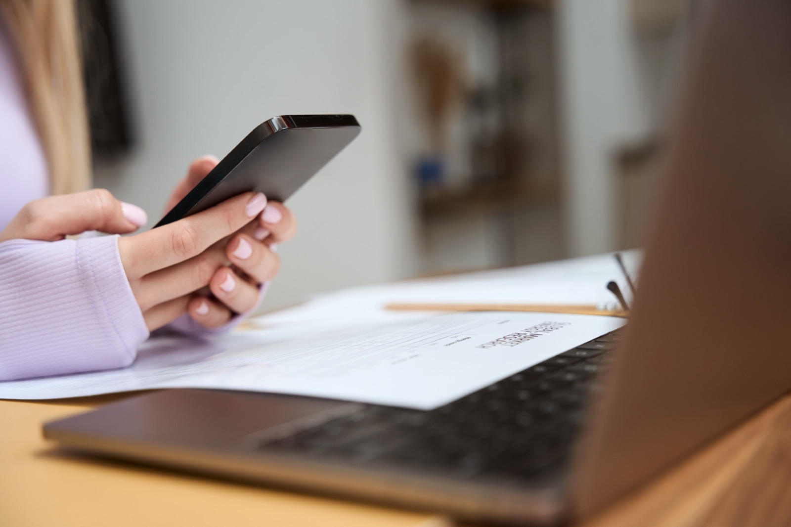 Hands holding a phone next to a laptop and papers on a desk