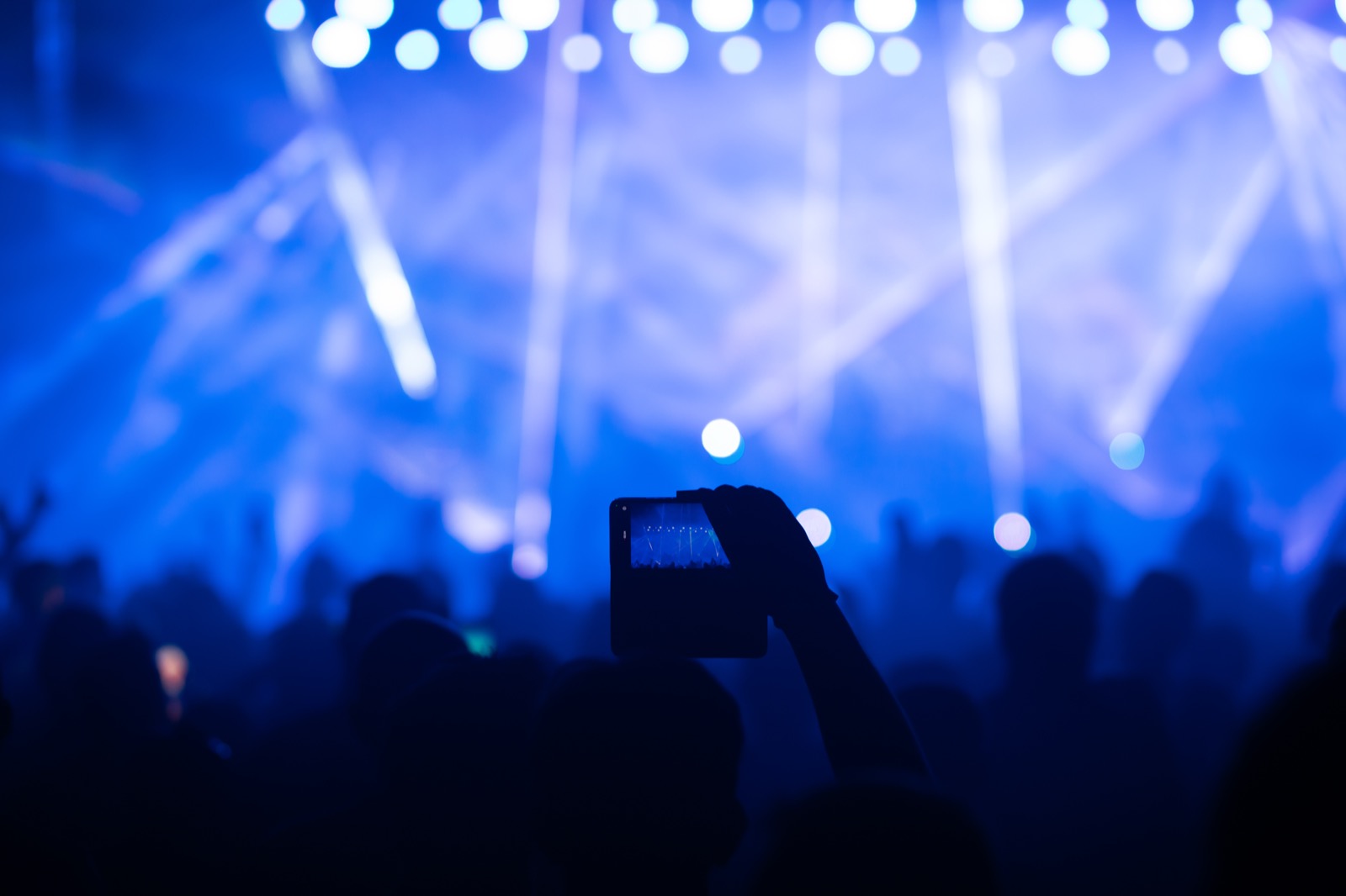 Silhouette of a hand holding up a phone to photograph stage lights