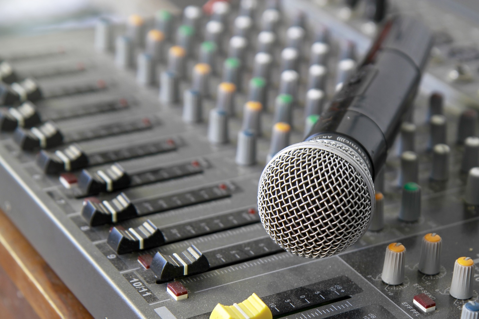 A microphone resting in front of a mixing console with cables visible