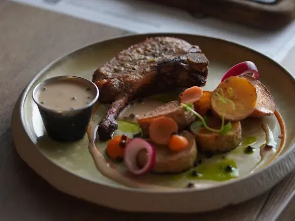 Tomahawk de porc cu cartofi copți, sos de piper verde și ardei copt