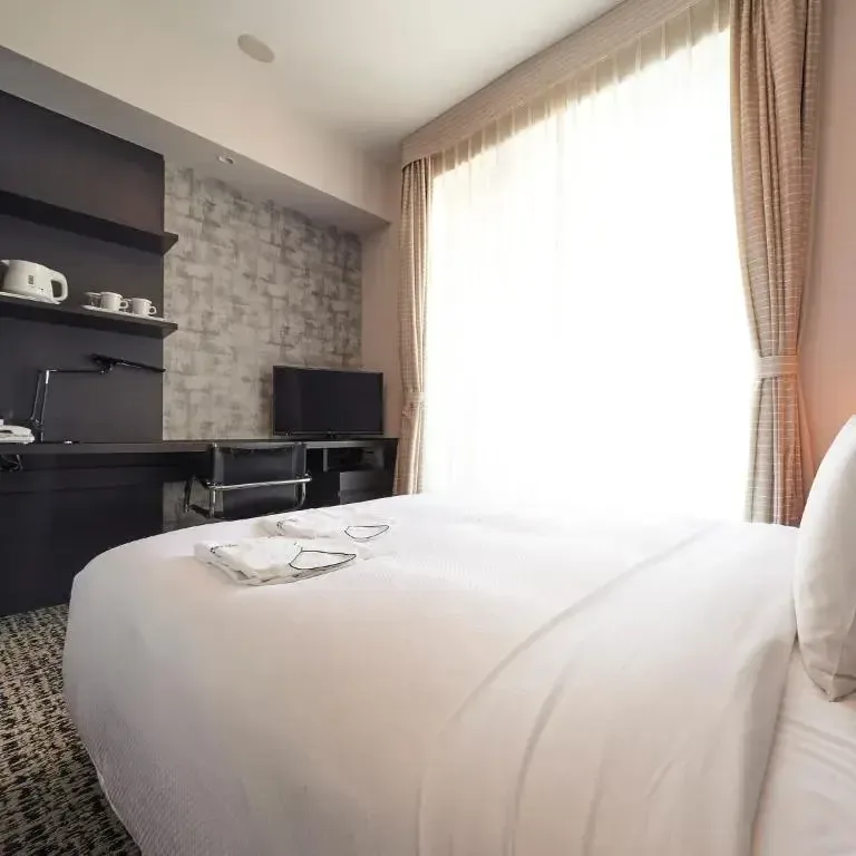 Modern hotel room with a neatly made bed, desk, television, and window with curtains in Japan.