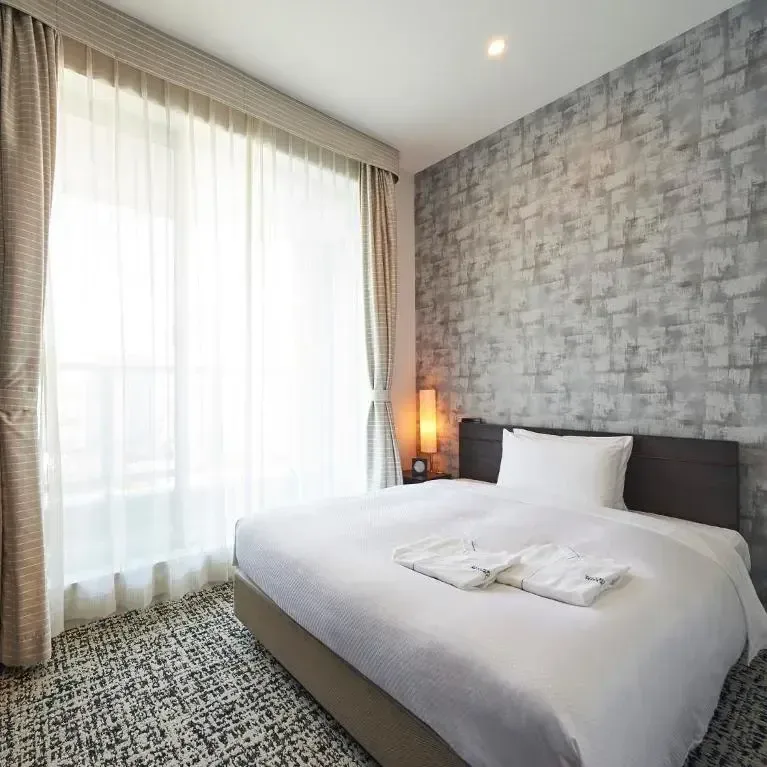 Bright and modern hotel bedroom with a neatly made bed, textured grey accent wall, and sheer curtains.