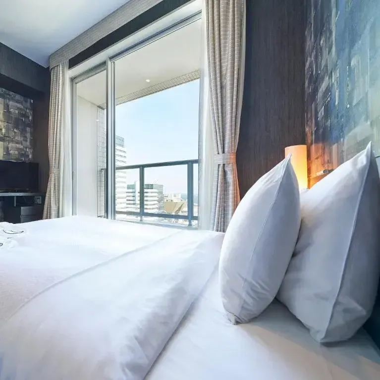 Modern hotel room featuring a comfortable white bed and a balcony overlooking the city skyline.