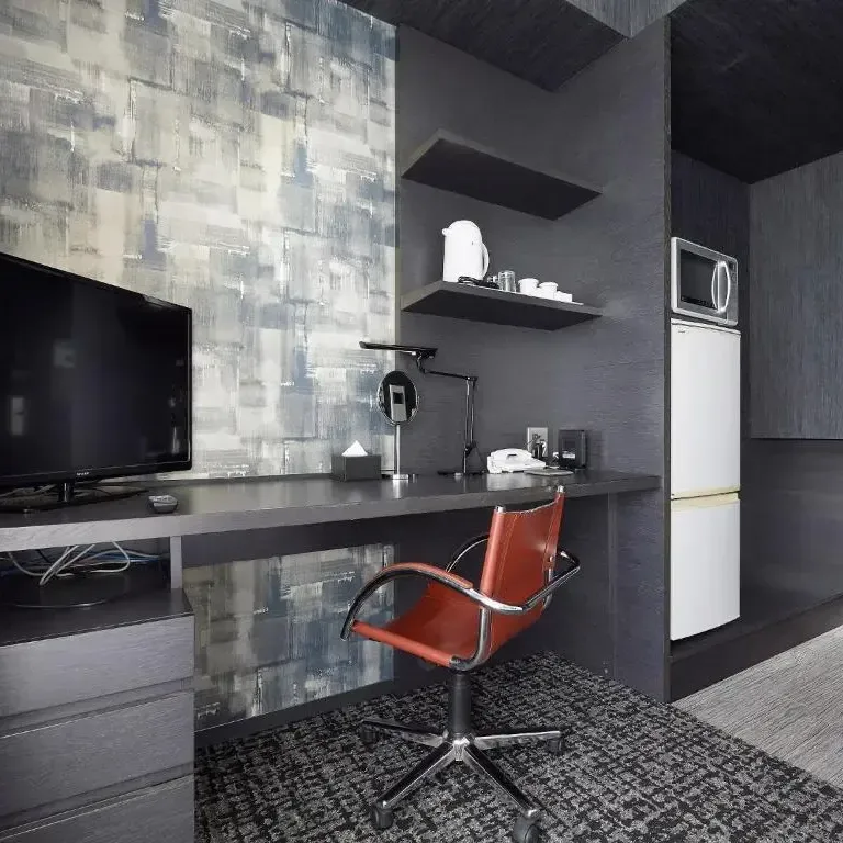 Modern hotel room desk with television, orange leather chair, shelving, and mini fridge in Tokyo accommodation.