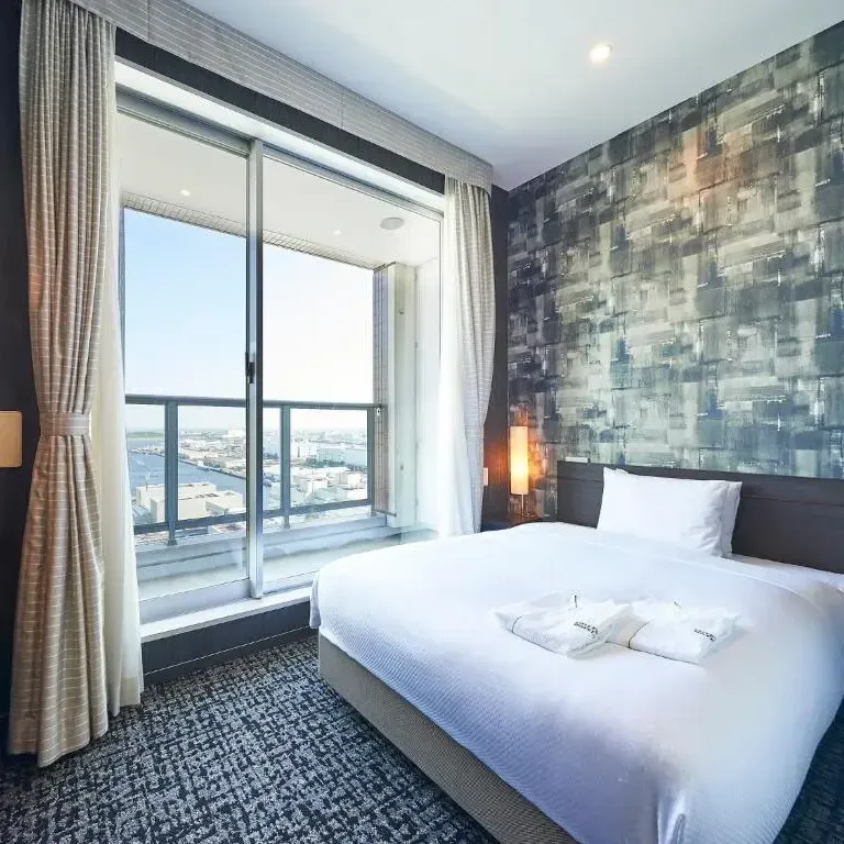 Modern hotel room in Tokyo featuring a large bed and expansive balcony overlooking the city harbor.