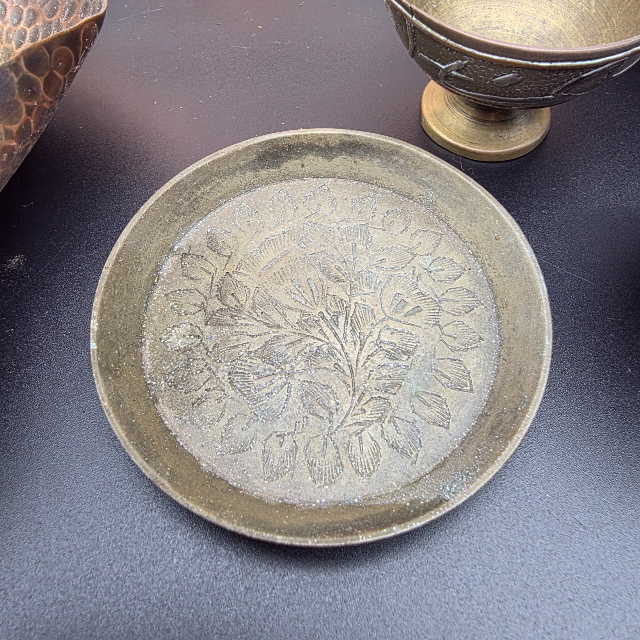 A diverse collection of vintage metalware, including a large copper wall plaque, a hammered copper dish, a small brass plate, two small brass cups, and a bronze/copper vase. - View 2