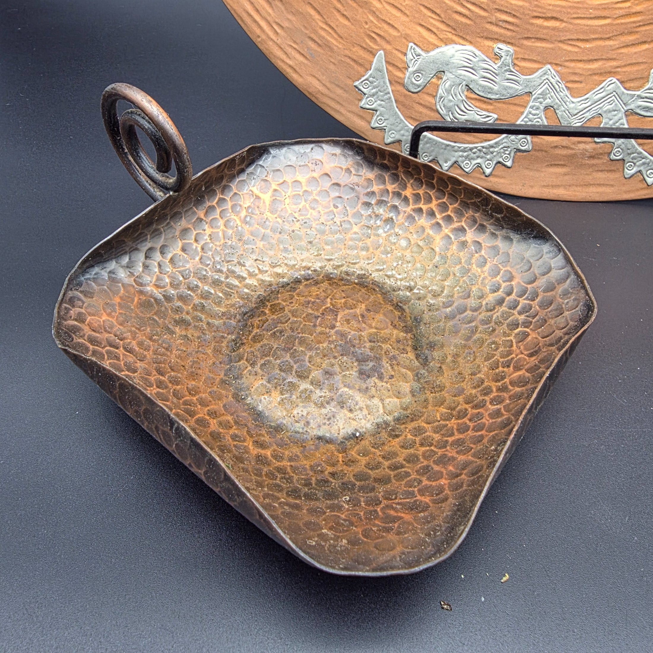 A diverse collection of vintage metalware, including a large copper wall plaque, a hammered copper dish, a small brass plate, two small brass cups, and a bronze/copper vase. - View 7