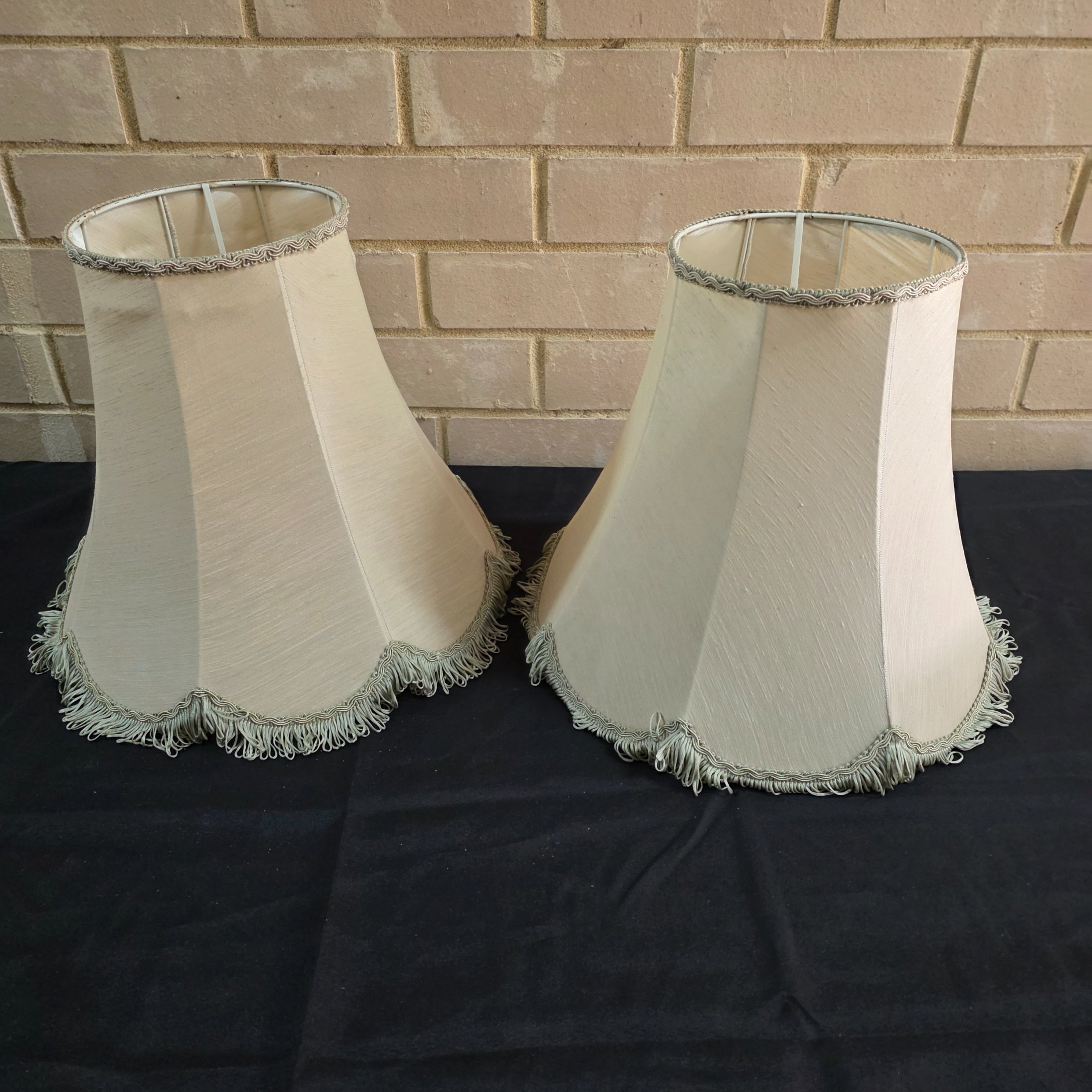 A pair of vintage bell-shaped lampshades, crafted from light fabric with ornate trim and fringe, suitable for traditional interior decor.