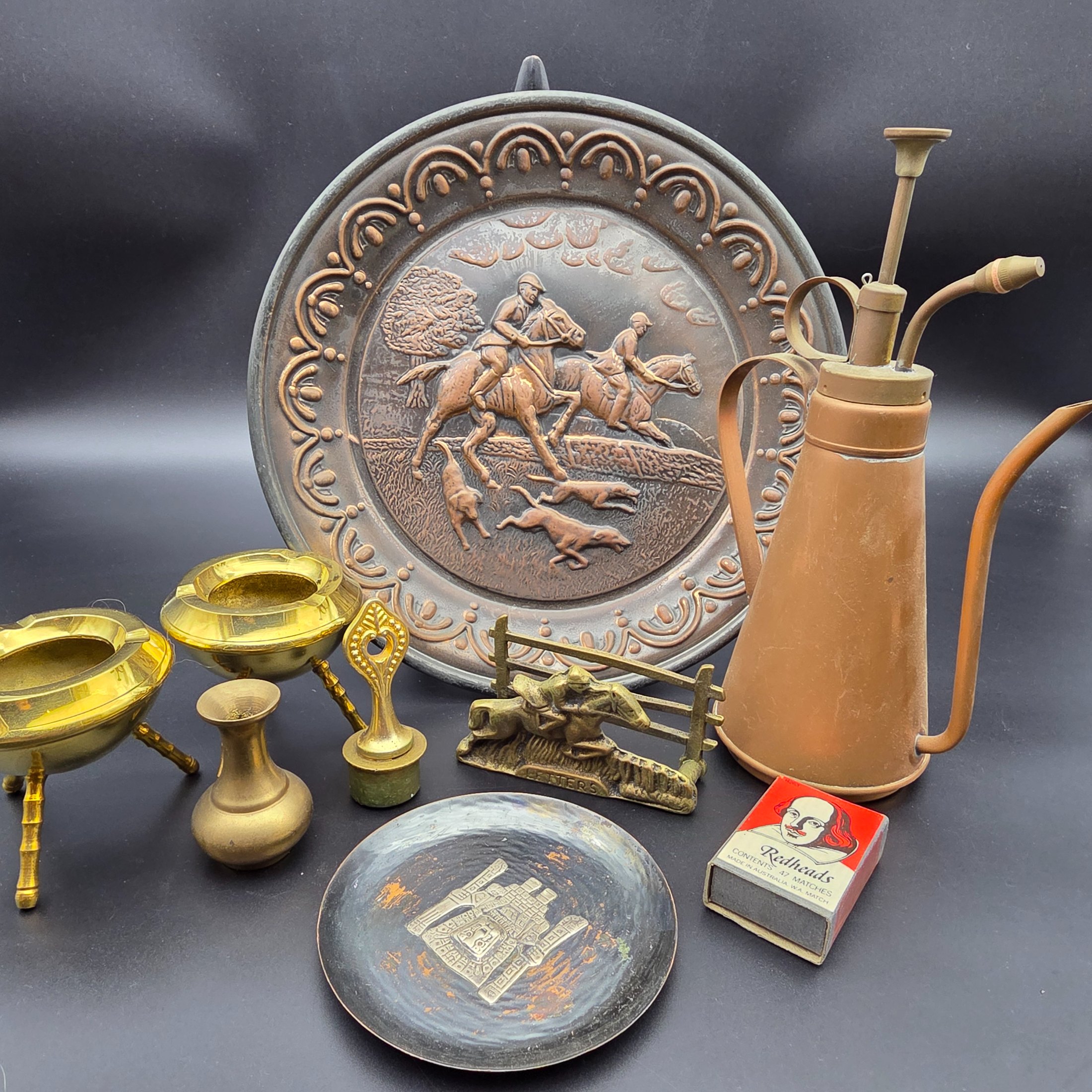 A curated collection of vintage metallic decorative sundries, primarily crafted from brass and copper, spanning mid to late 20th-century origins, including an embossed wall plate, a plant mister, letter holder, ashtrays, a vase, and a small dish.