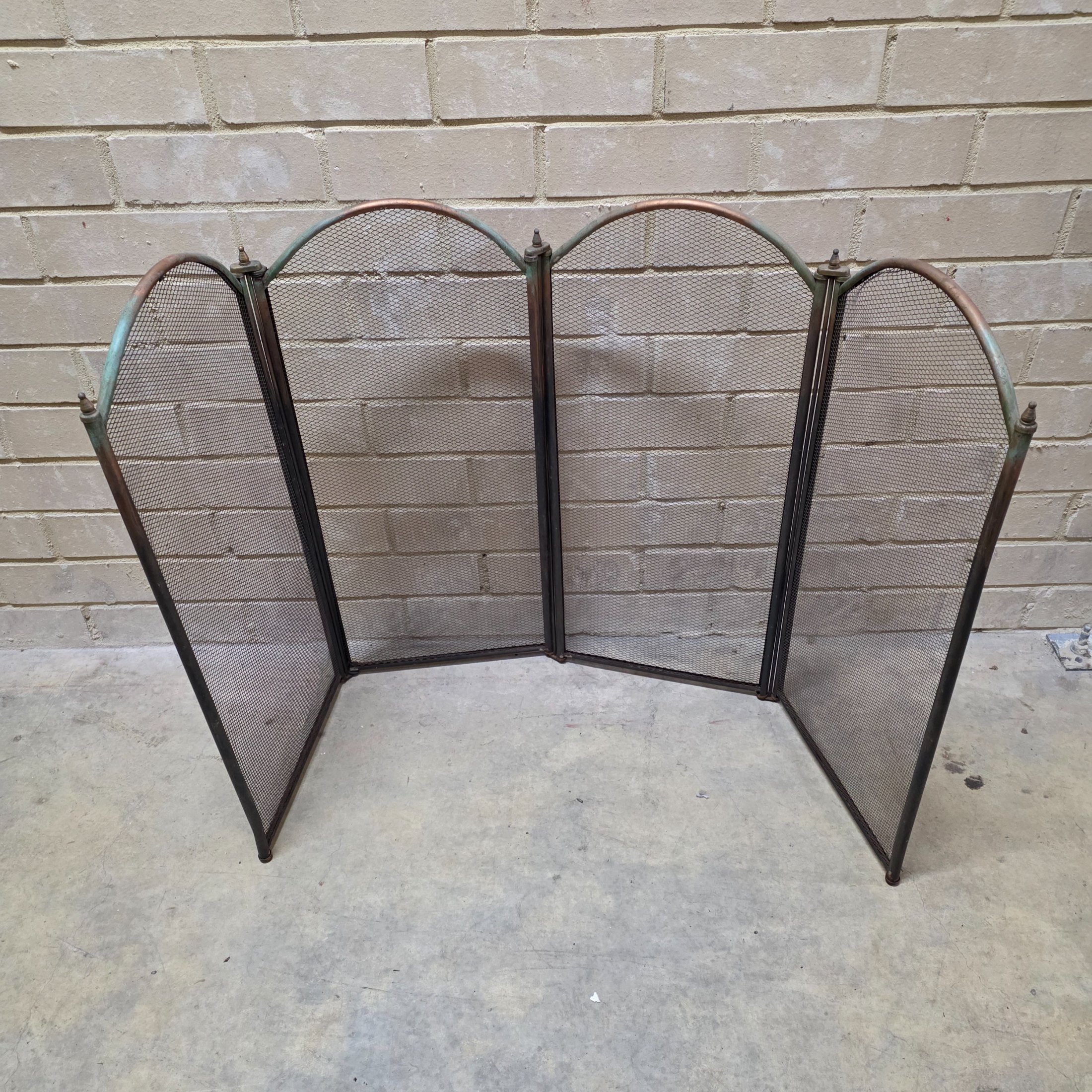 A vintage four-panel brass and mesh fireplace screen, designed to protect from sparks while adding decorative appeal to a hearth.