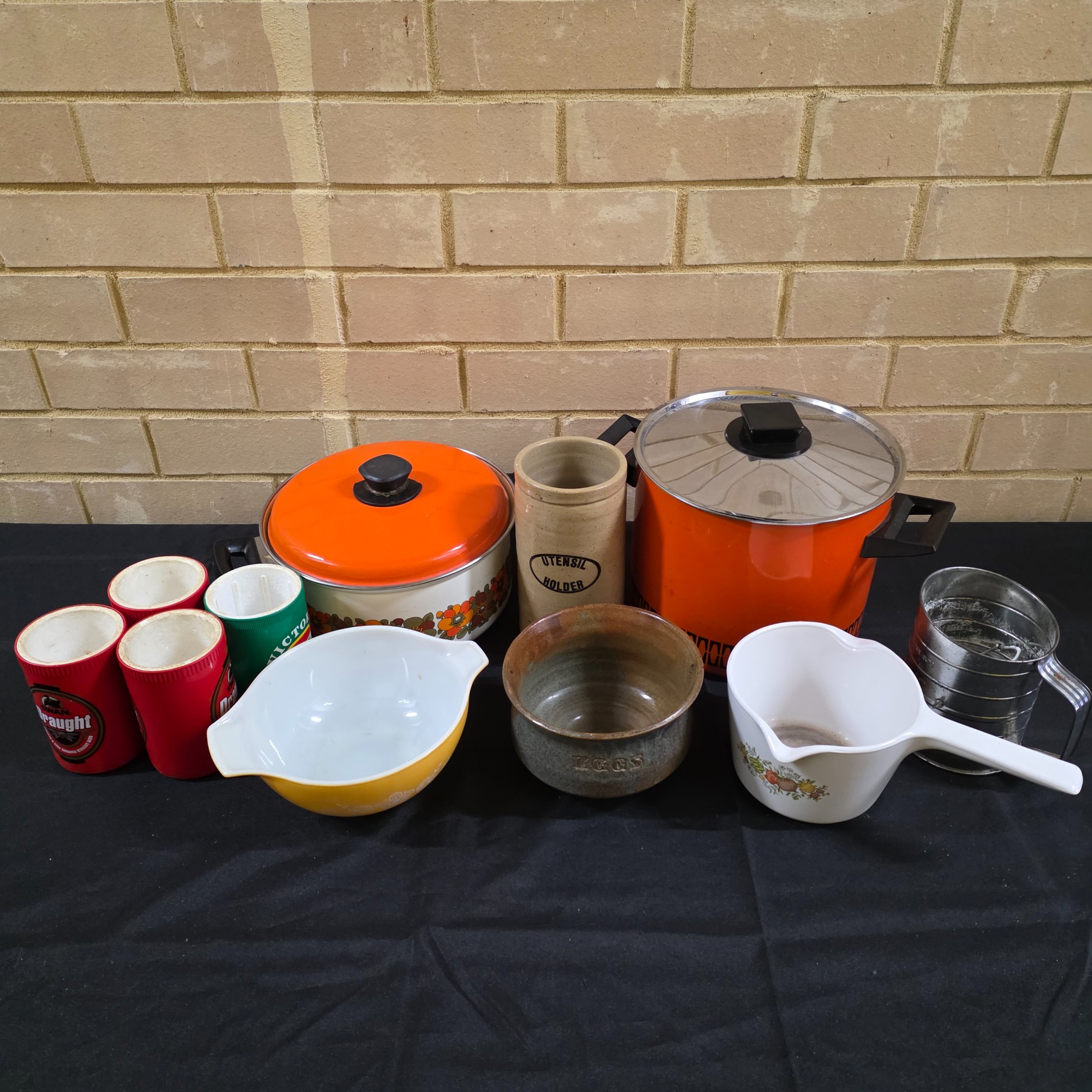 A varied collection of vintage kitchenware and homewares, showcasing mid-century design and practical items, including enamel pots, ceramic and stoneware pieces, and Australian beer coolers.