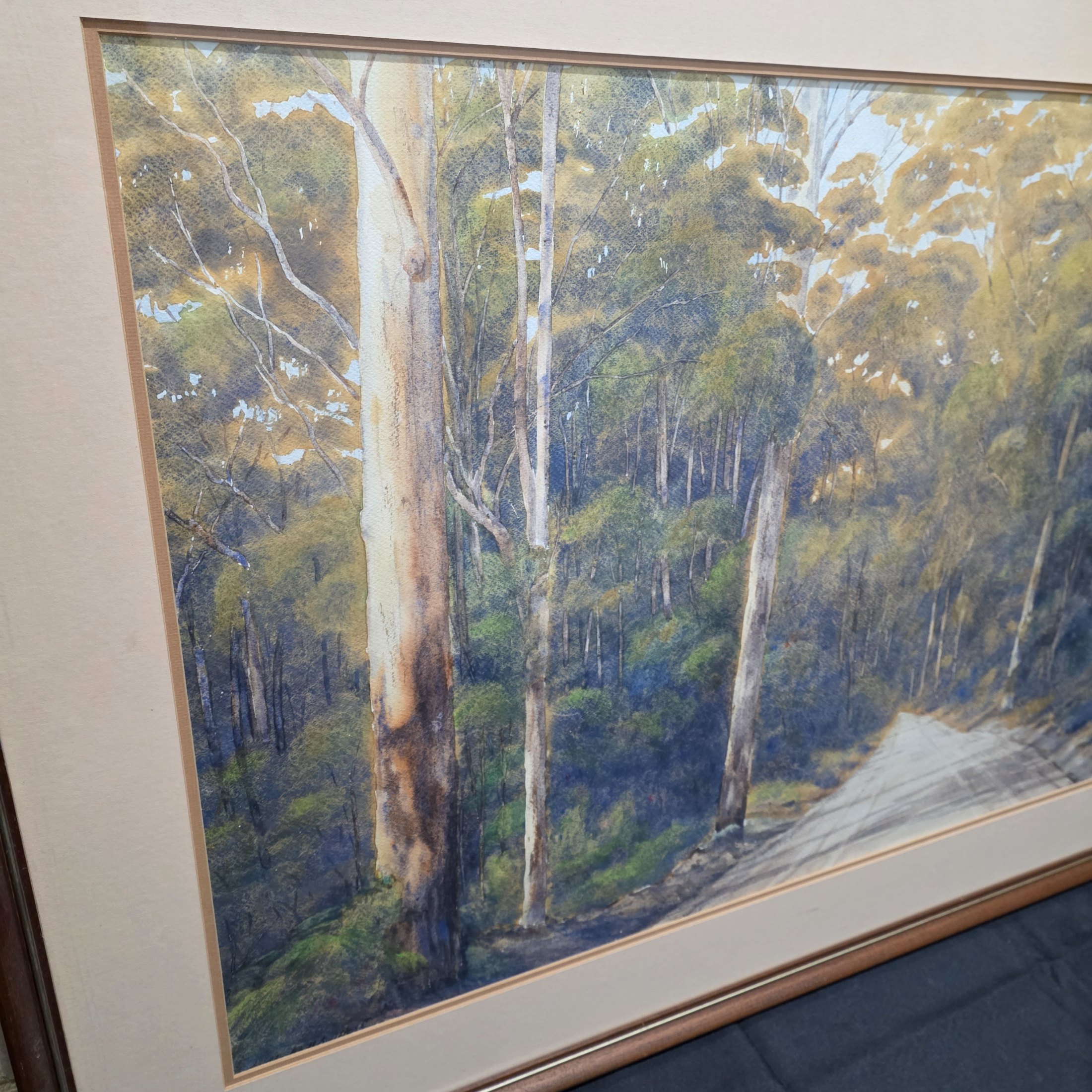A framed original watercolour painting depicting a tranquil Australian bush scene with a dirt road winding through tall eucalypt trees, signed 'N. A. H.' and dated 1984. - View 2