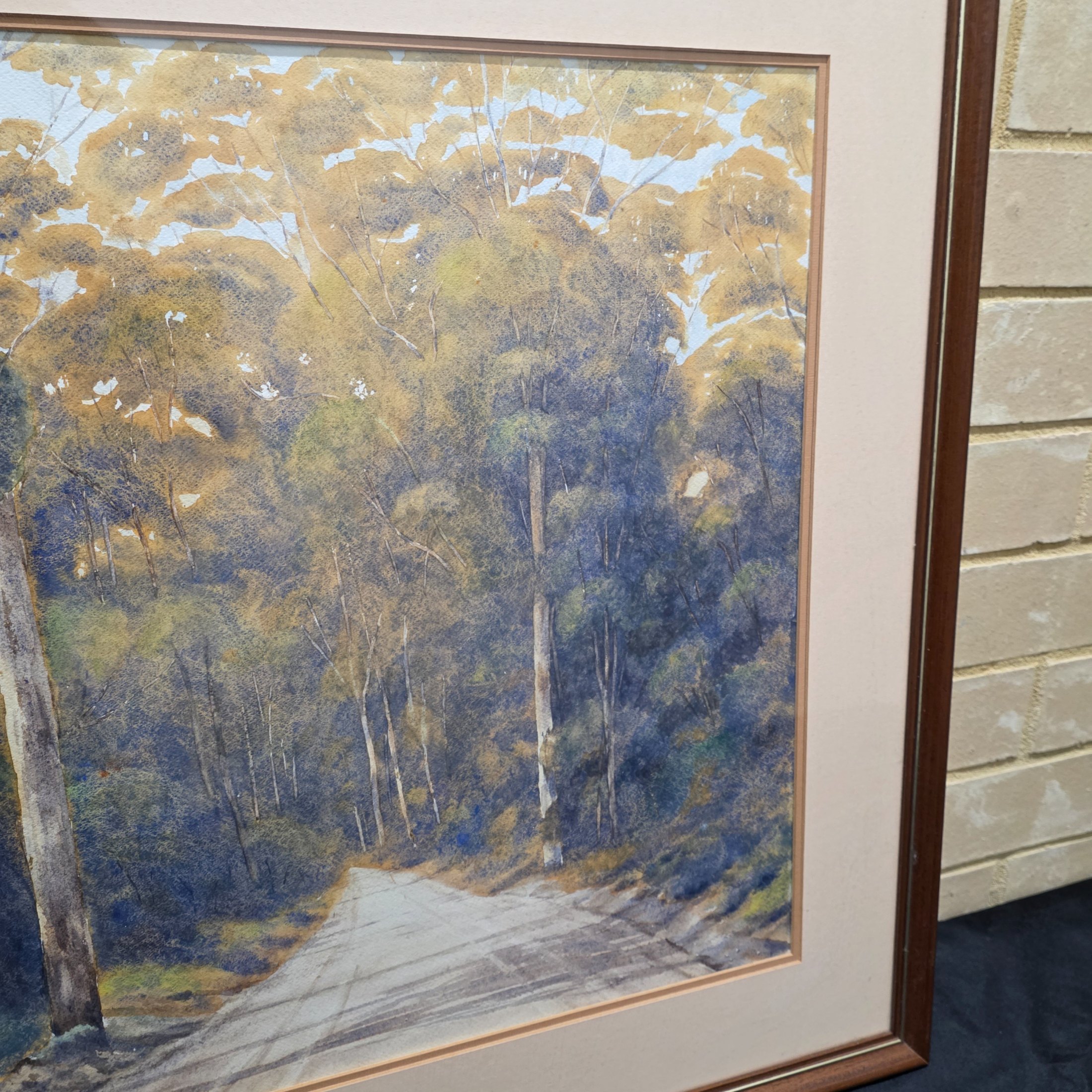 A framed original watercolour painting depicting a tranquil Australian bush scene with a dirt road winding through tall eucalypt trees, signed 'N. A. H.' and dated 1984. - View 5