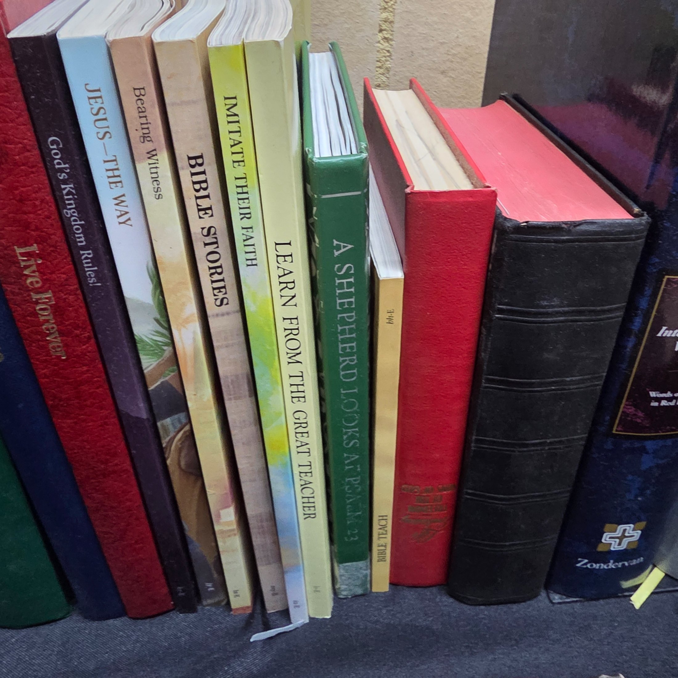 A large collection of mixed religious books and Bibles, including various translations, study guides, and annual publications, presented in a cardboard box and arranged on a surface. - View 3