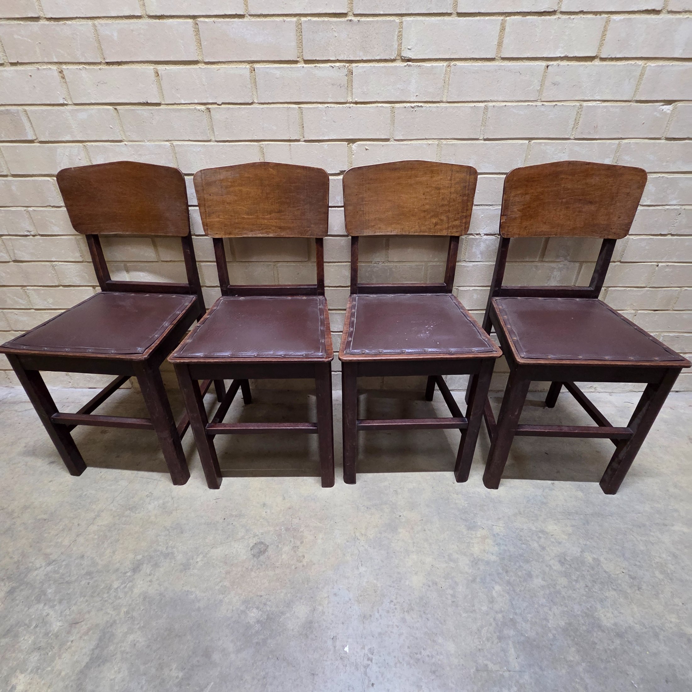 A set of four vintage dark wood dining chairs, featuring a simple, robust design and dark brown studded faux leather seats.