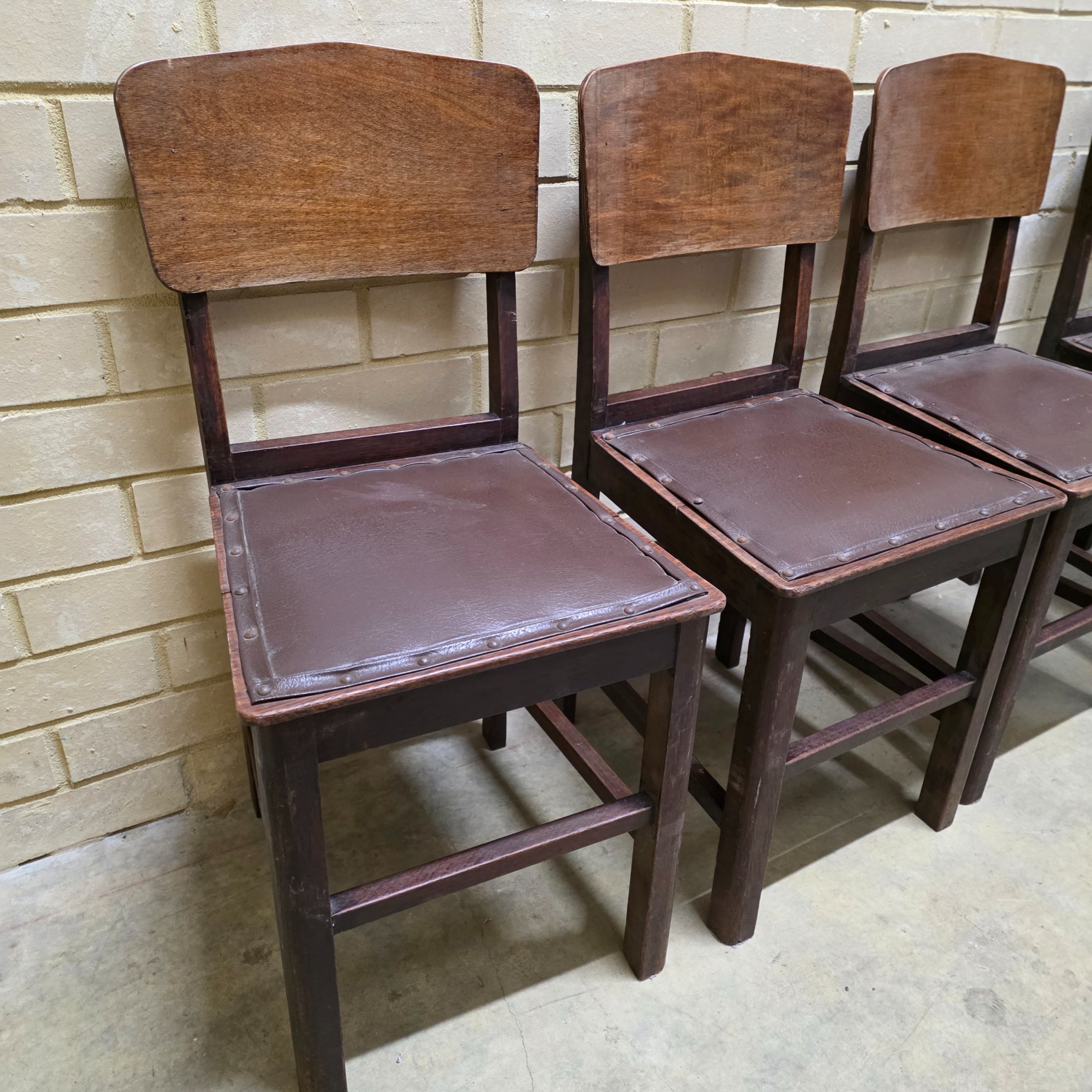 A set of four vintage dark wood dining chairs, featuring a simple, robust design and dark brown studded faux leather seats. - View 2