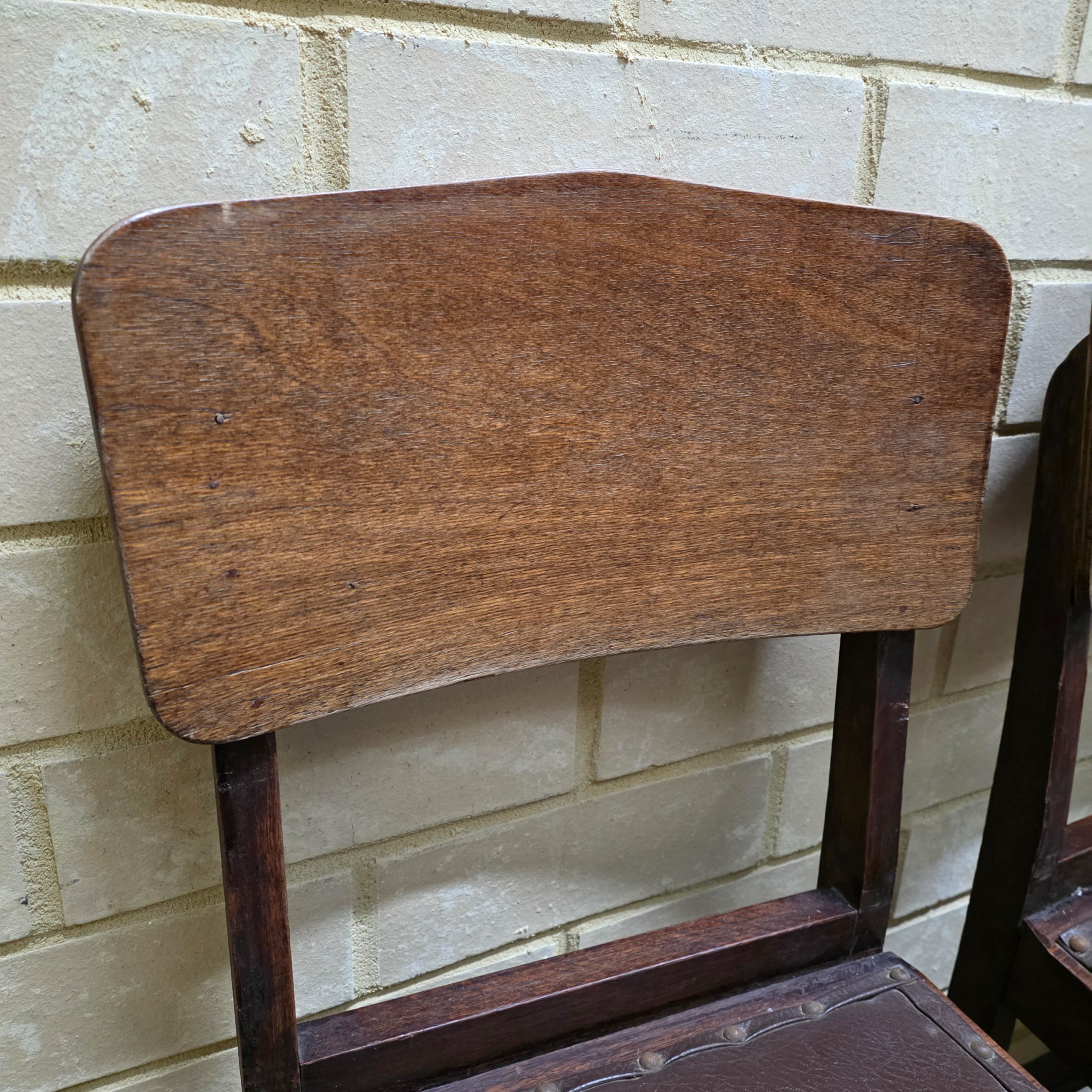 A set of four vintage dark wood dining chairs, featuring a simple, robust design and dark brown studded faux leather seats. - View 4