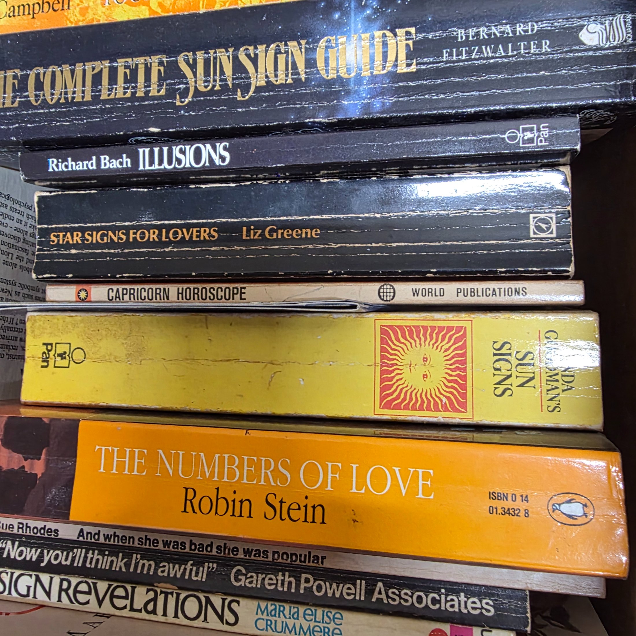 A cardboard box filled with approximately two dozen used books, predominantly on astrology, numerology, and self-help topics. - View 4