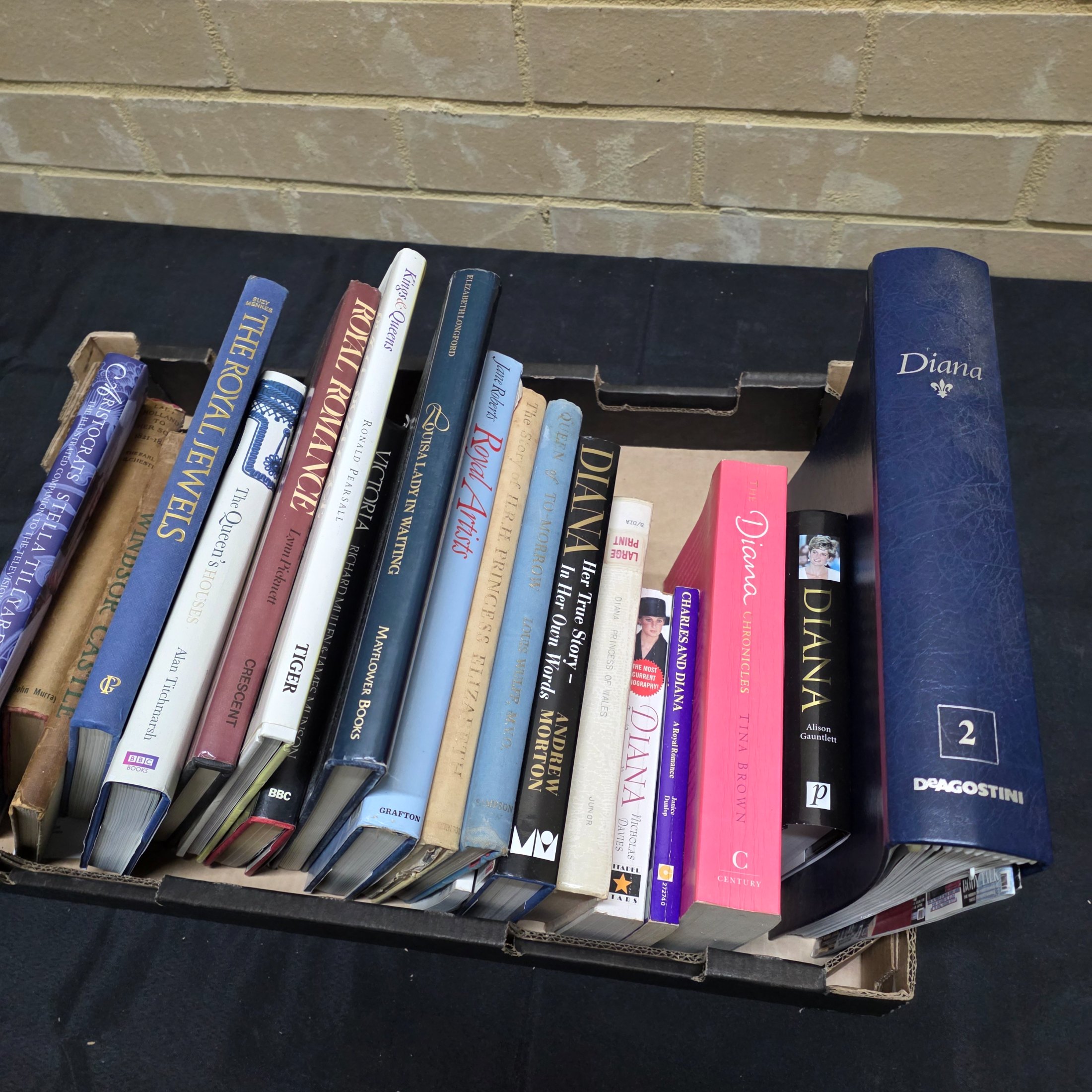 A cardboard box filled with approximately two dozen assorted books primarily focused on British royalty, including biographies of Princess Diana and historical accounts of castles and queens.