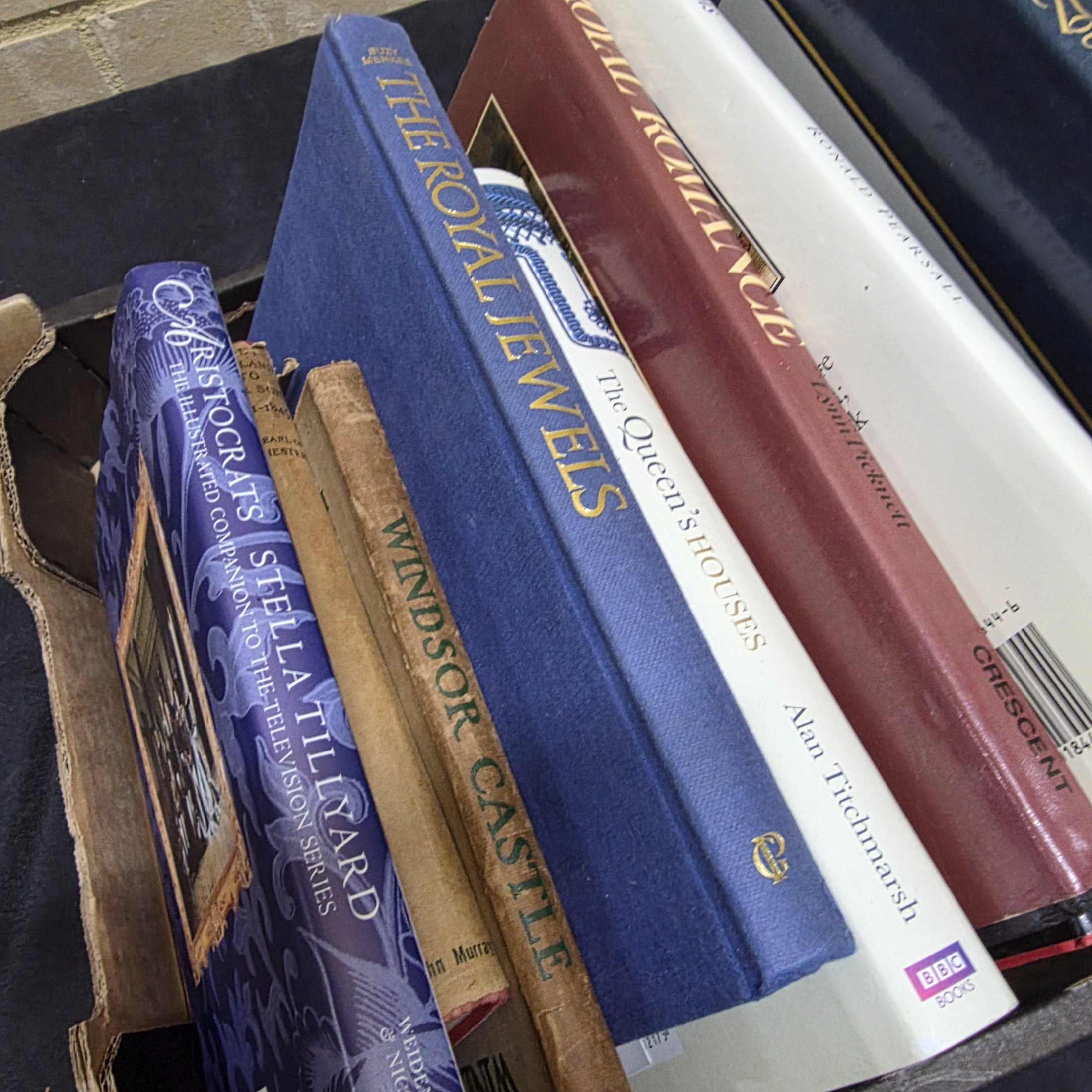 A cardboard box filled with approximately two dozen assorted books primarily focused on British royalty, including biographies of Princess Diana and historical accounts of castles and queens. - View 4