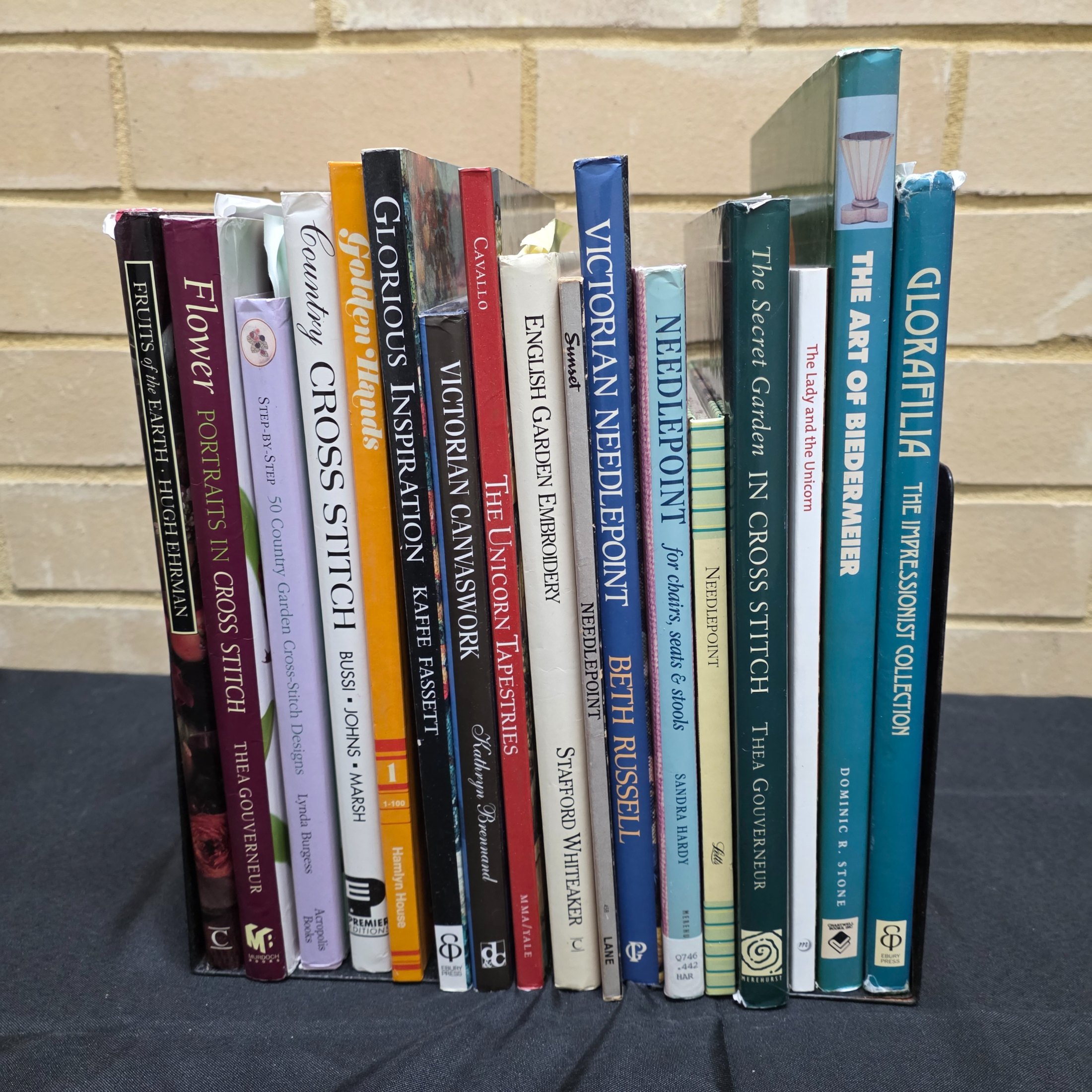 A collection of approximately 18 reference books focusing on needlecrafts and historical design, including titles on cross-stitch, needlepoint, tapestry, and Biedermeier art.