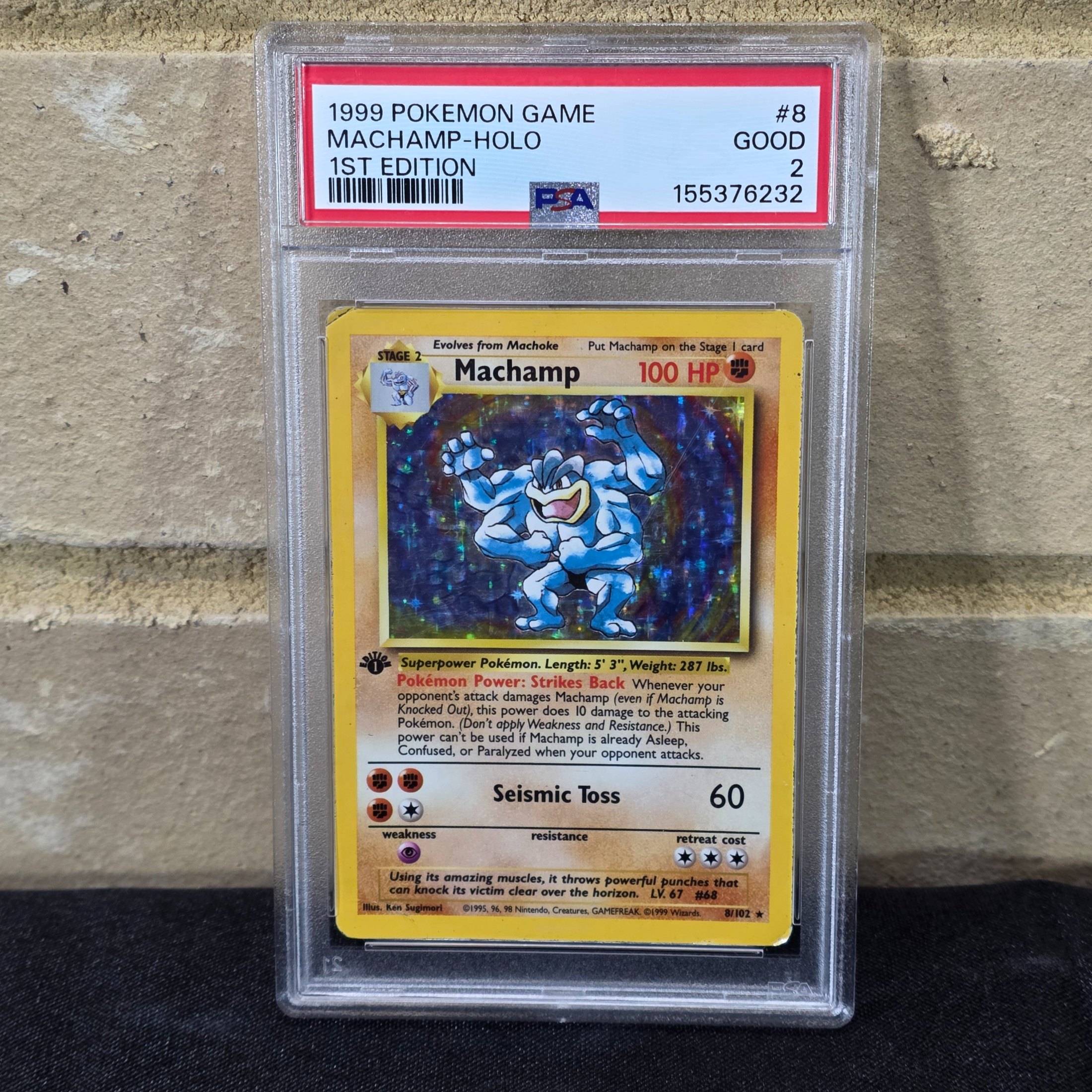 A 1999 Pokémon Game Machamp-Holo 1st Edition trading card, professionally graded PSA GOOD 2, displayed in a protective slab.