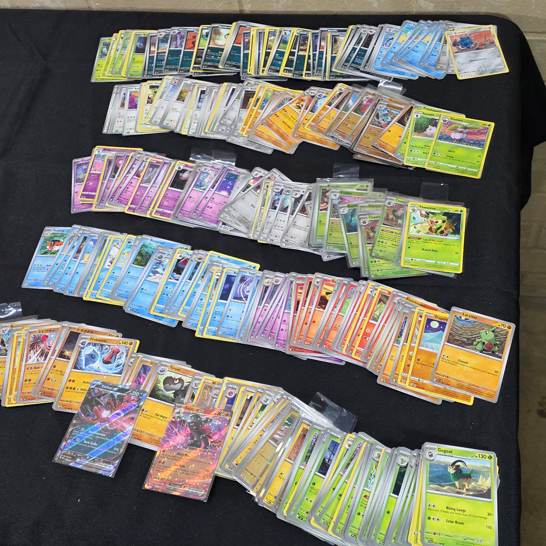 A large collection of Japanese and English Pokemon trading cards, featuring a diverse range of characters and card types spread across a black surface.