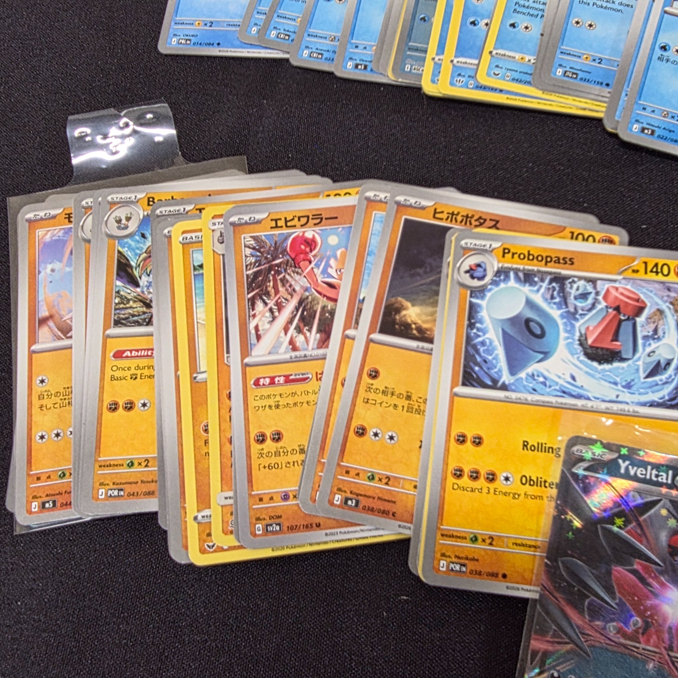 A large collection of Japanese and English Pokemon trading cards, featuring a diverse range of characters and card types spread across a black surface. - View 2