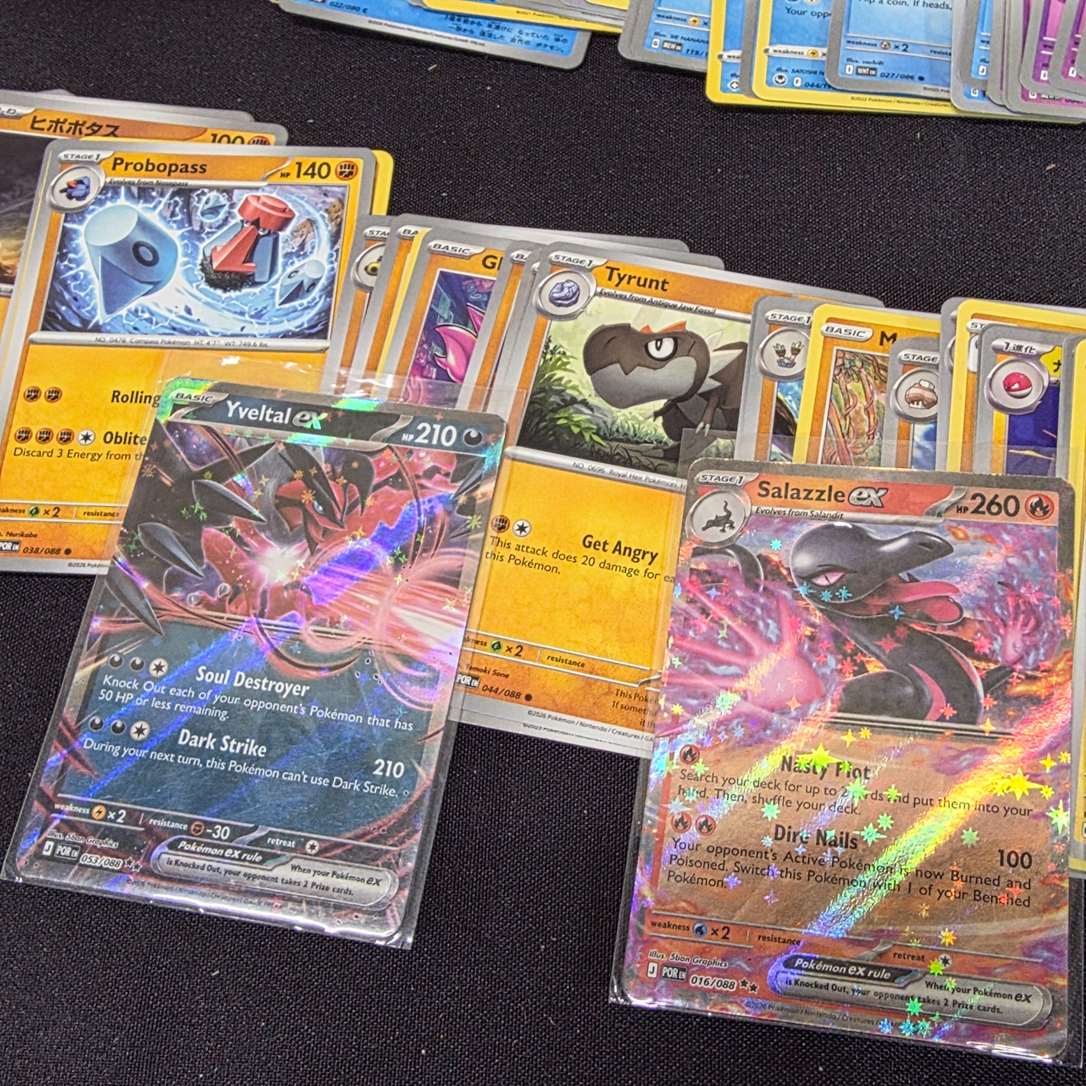 A large collection of Japanese and English Pokemon trading cards, featuring a diverse range of characters and card types spread across a black surface. - View 3