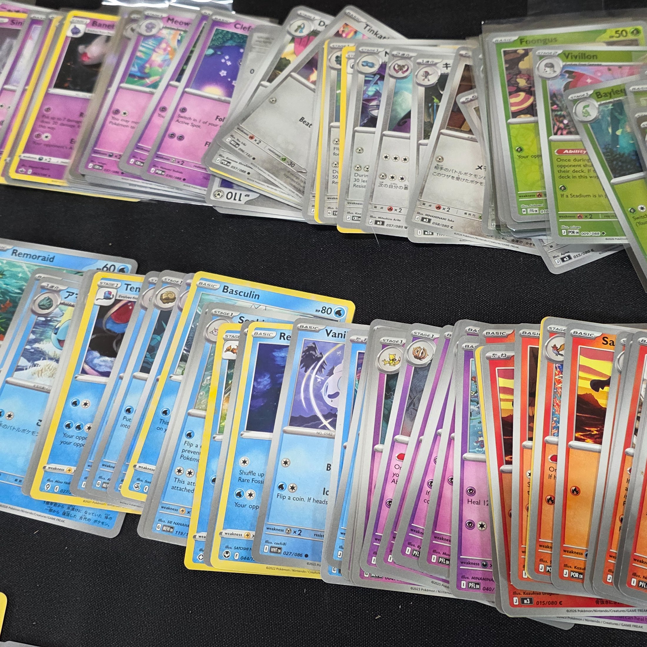 A large collection of Japanese and English Pokemon trading cards, featuring a diverse range of characters and card types spread across a black surface. - View 6