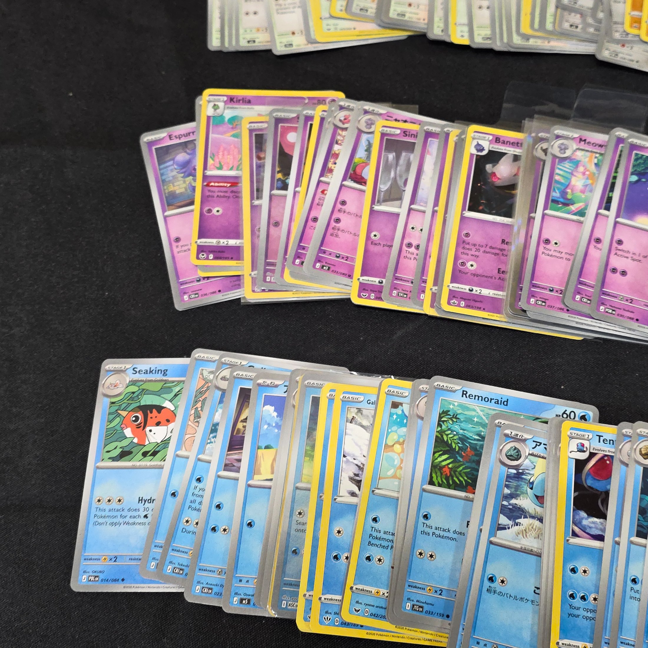 A large collection of Japanese and English Pokemon trading cards, featuring a diverse range of characters and card types spread across a black surface. - View 7