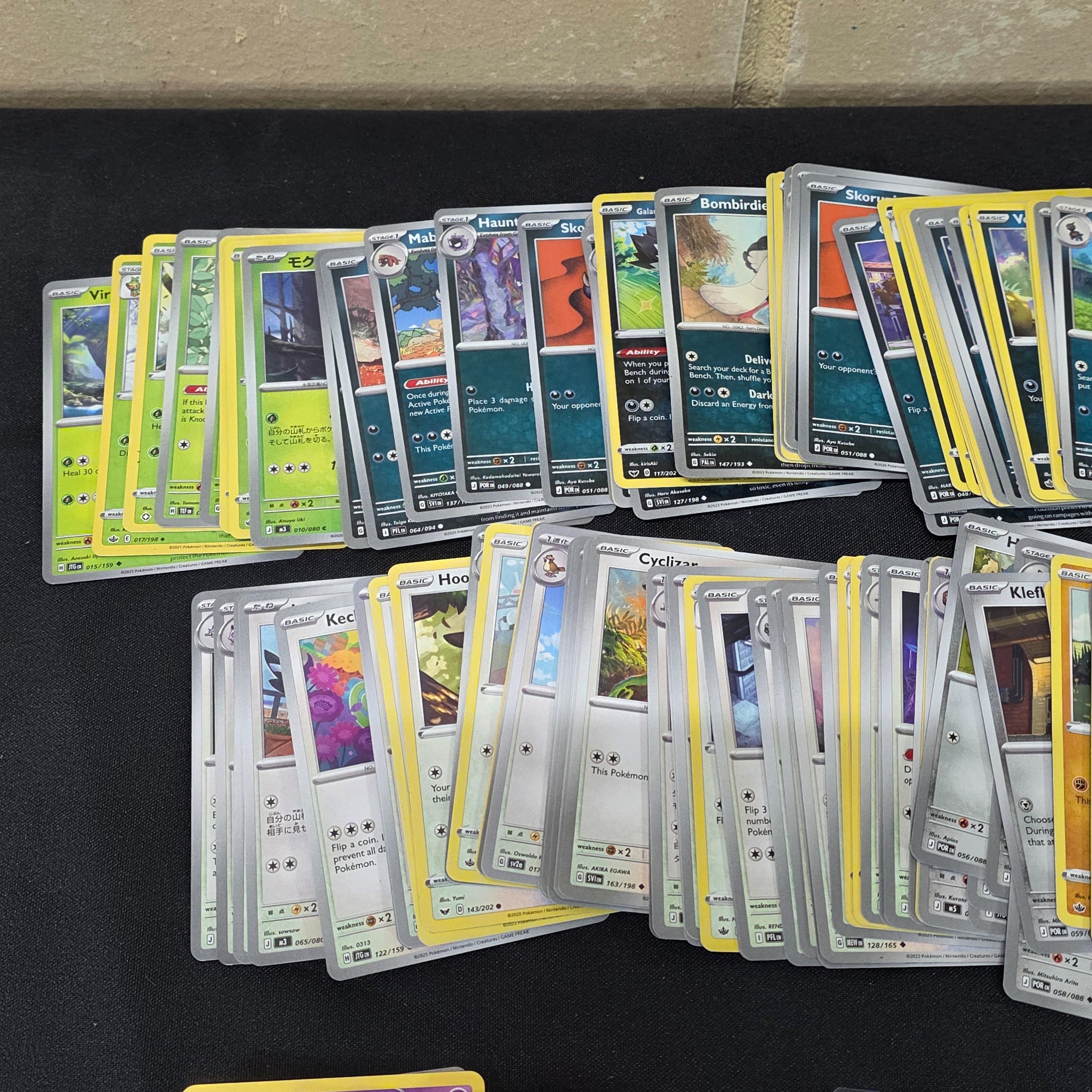 A large collection of Japanese and English Pokemon trading cards, featuring a diverse range of characters and card types spread across a black surface. - View 8