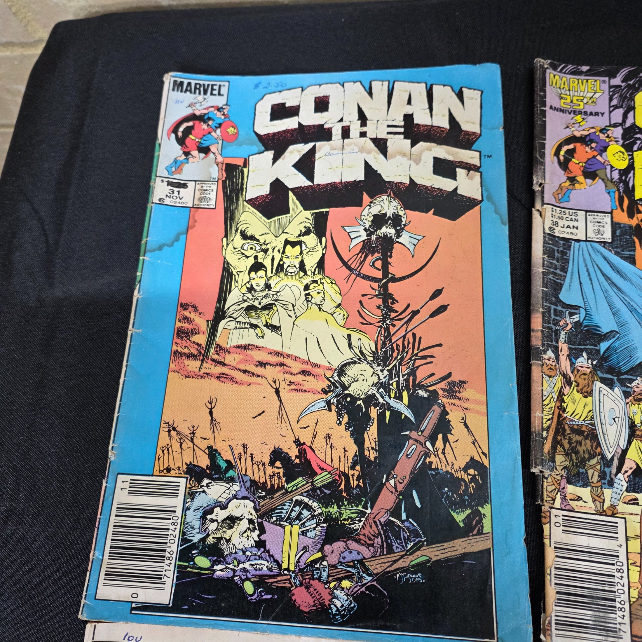 A collection of vintage Marvel 'Conan the King' and 'Conan the Barbarian' comic books from the 1980s, displayed on a black surface against a brick wall. - View 2