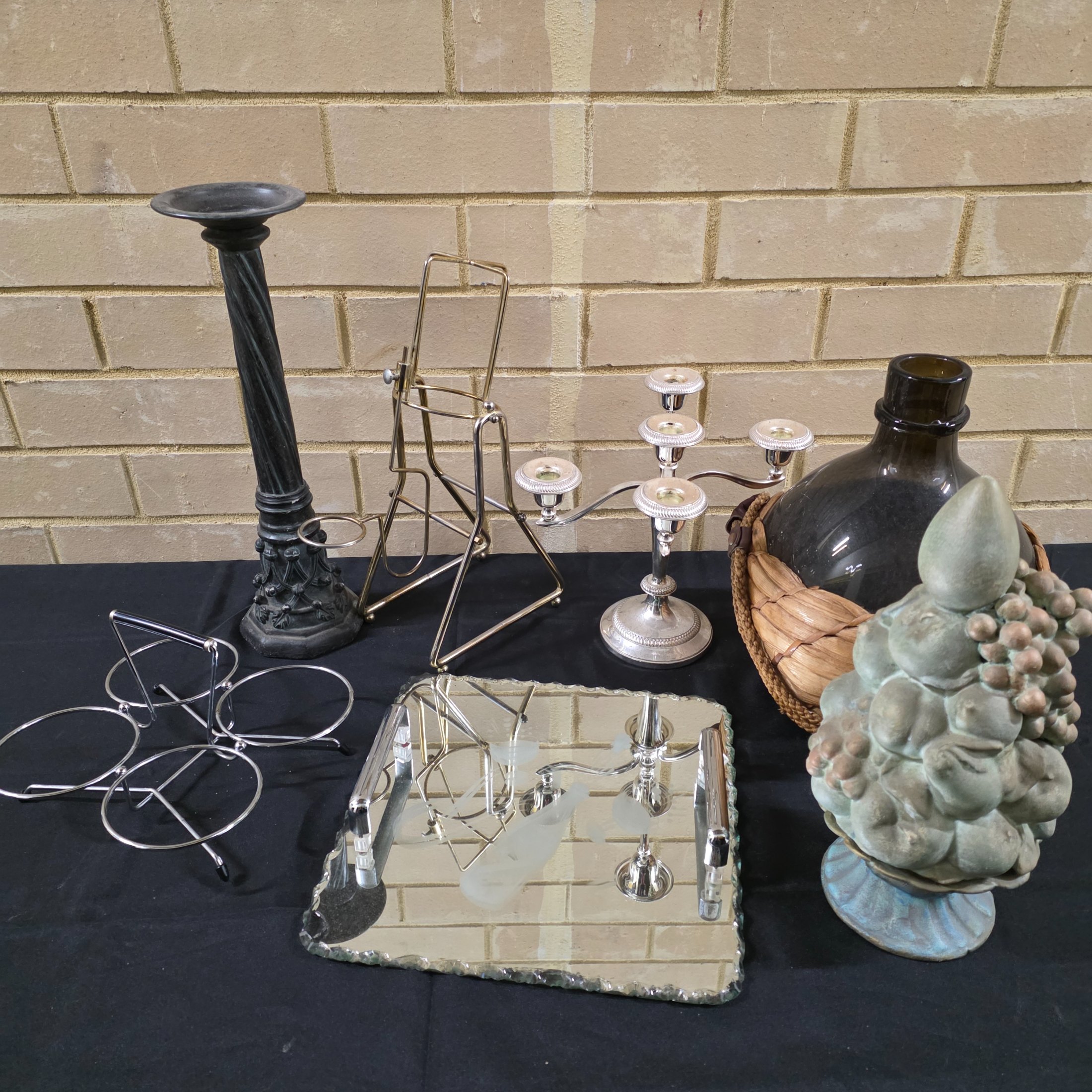 A varied collection of vintage homewares featuring a dark metal candlestick, a silver-plated candelabra, a mirrored tray, and several other decorative and functional pieces.