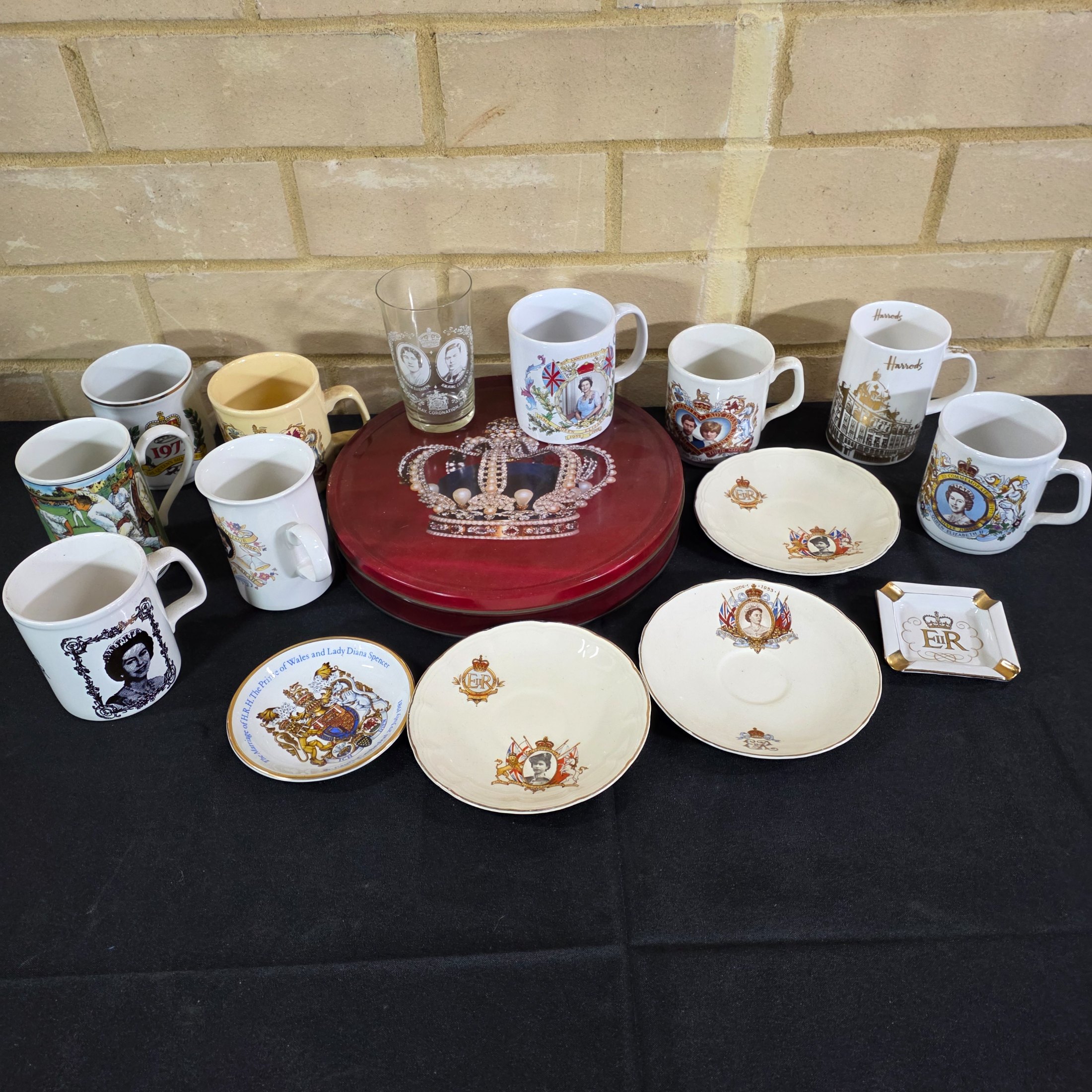 A diverse collection of commemorative ceramics, decorative mugs, and various household sundries from the mid to late 20th century, including royal memorabilia, novelty mugs, a vintage wax jar, and a tea tin.