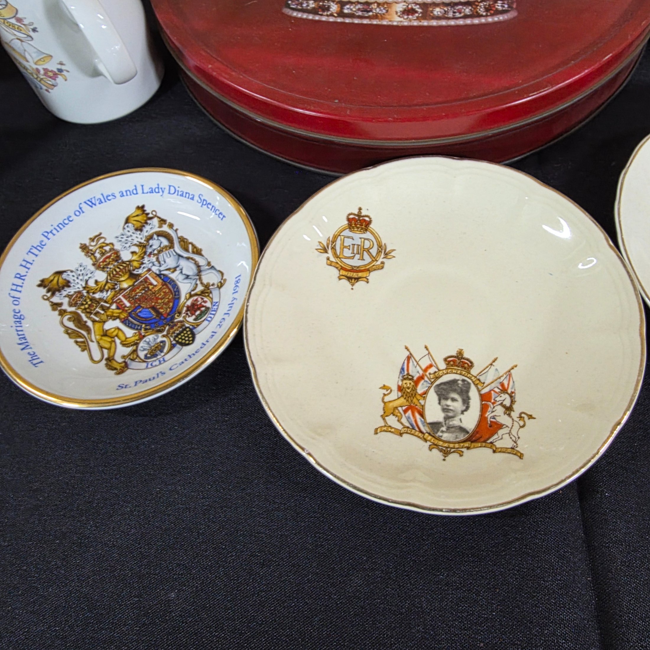 A diverse collection of commemorative ceramics, decorative mugs, and various household sundries from the mid to late 20th century, including royal memorabilia, novelty mugs, a vintage wax jar, and a tea tin. - View 3
