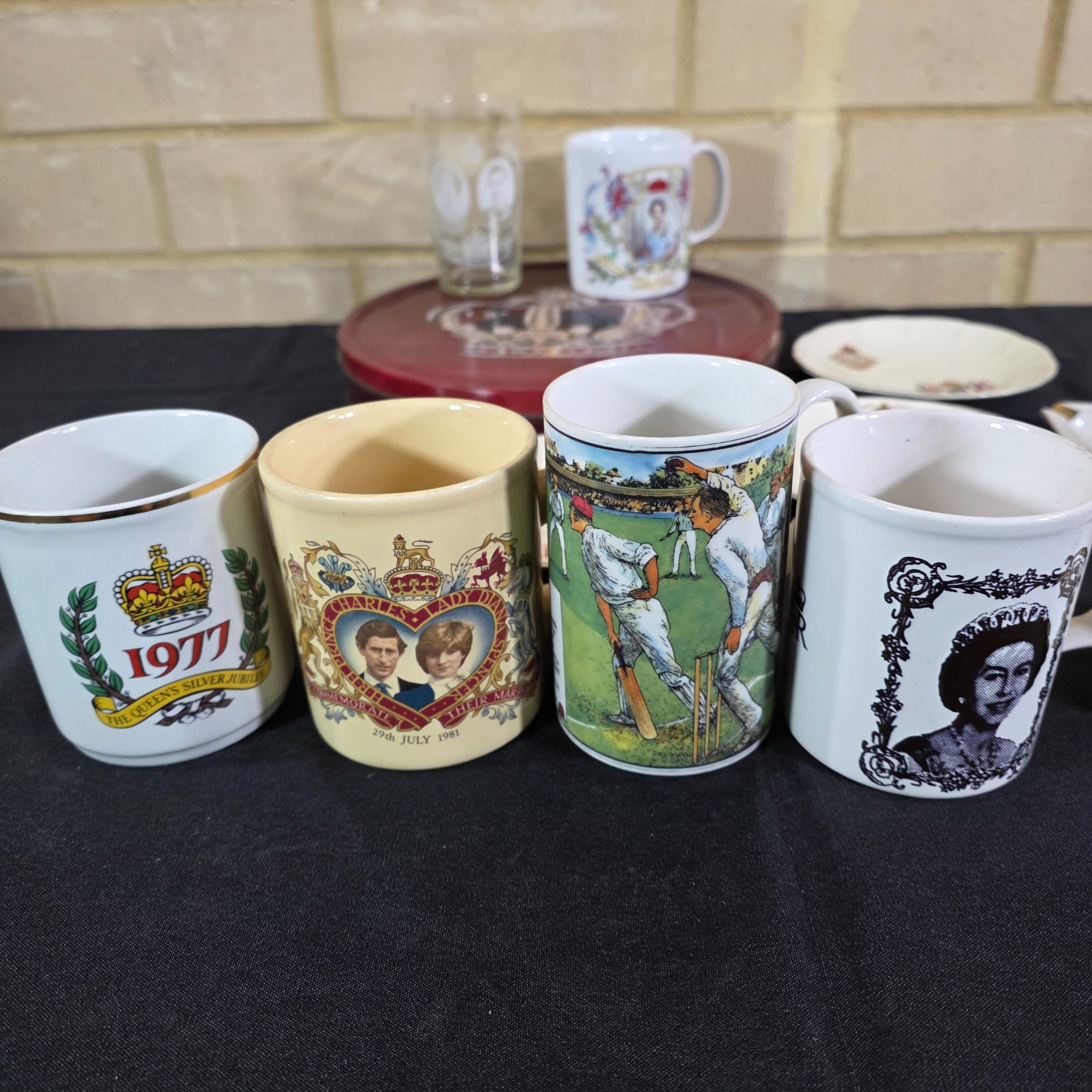 A diverse collection of commemorative ceramics, decorative mugs, and various household sundries from the mid to late 20th century, including royal memorabilia, novelty mugs, a vintage wax jar, and a tea tin. - View 6