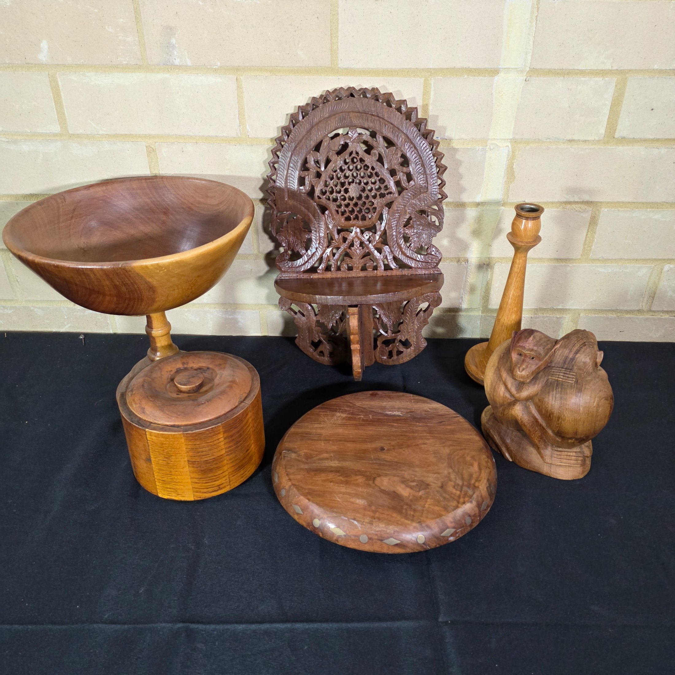 A collection of vintage wooden homewares including a pedestal bowl, lidded container, carved monkey figure, candlestick, wall shelf, and a round trivet.