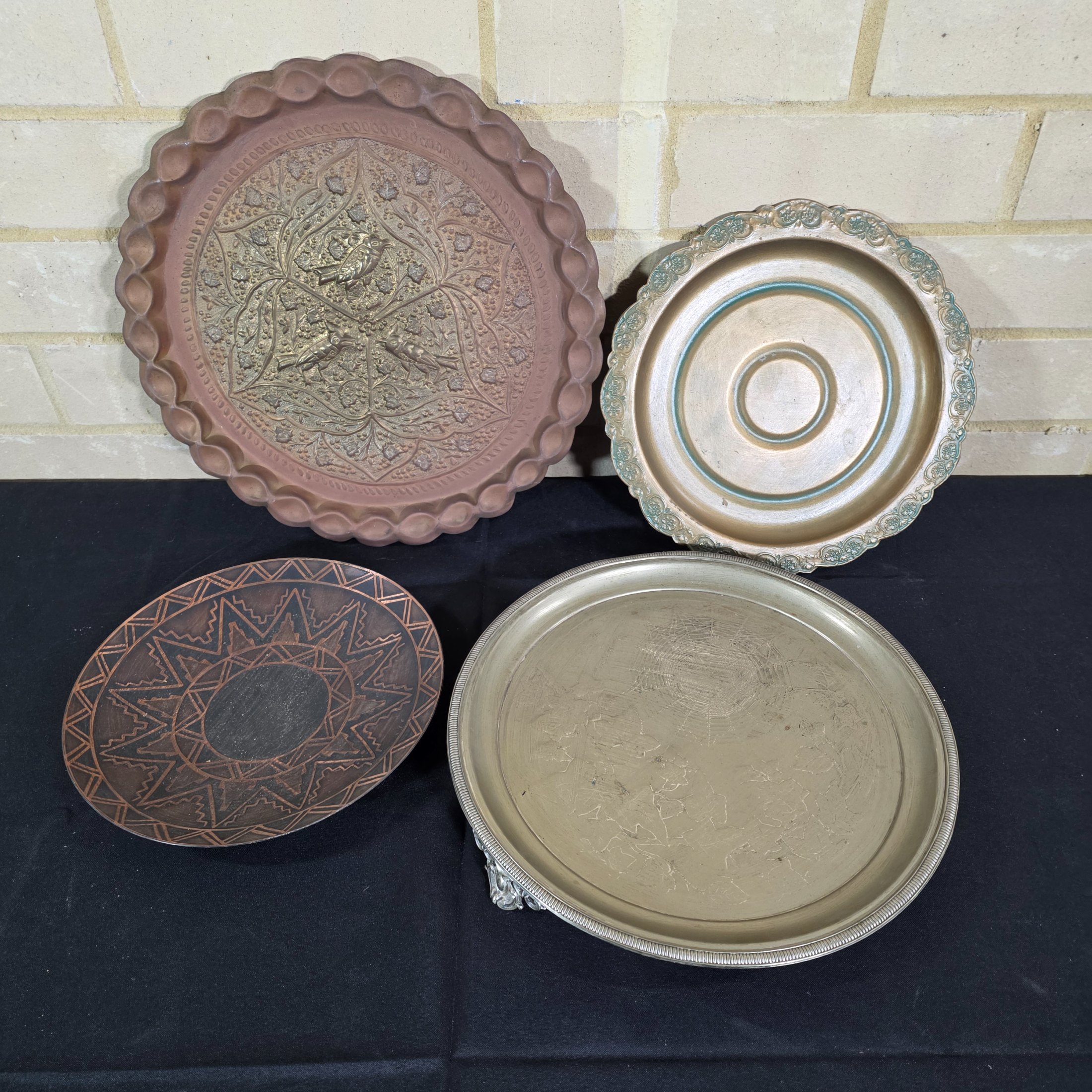 A collection of four assorted decorative metal plates and trays, featuring various embossed and etched designs, suitable for vintage decor.