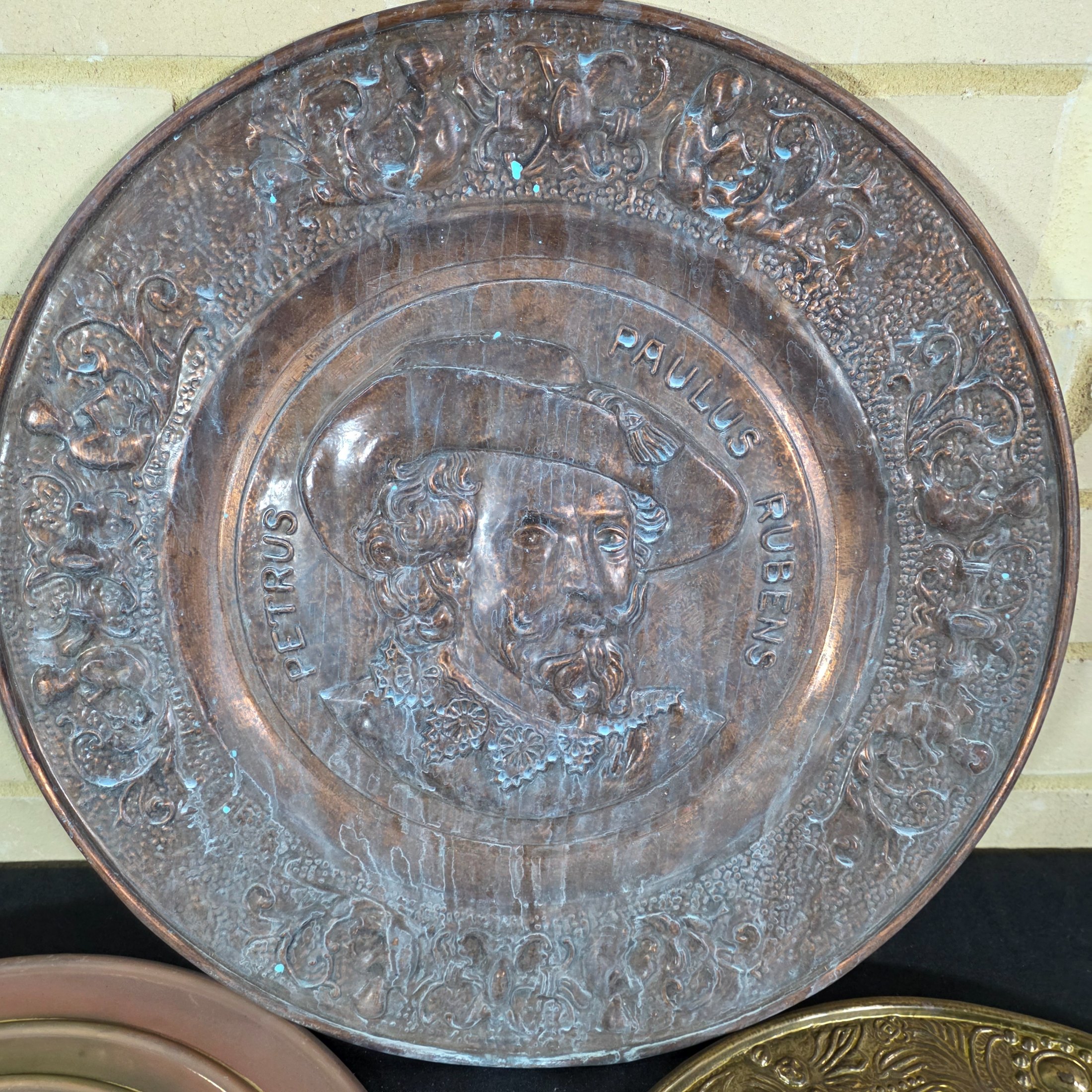 A collection of four vintage embossed metal wall plaques, comprising a large copper-toned plaque featuring a portrait of Peter Paul Rubens, two brass-toned plaques depicting fox hunting and horse-drawn carriage scenes, and a smaller copper-toned plaque with a tavern scene. - View 2