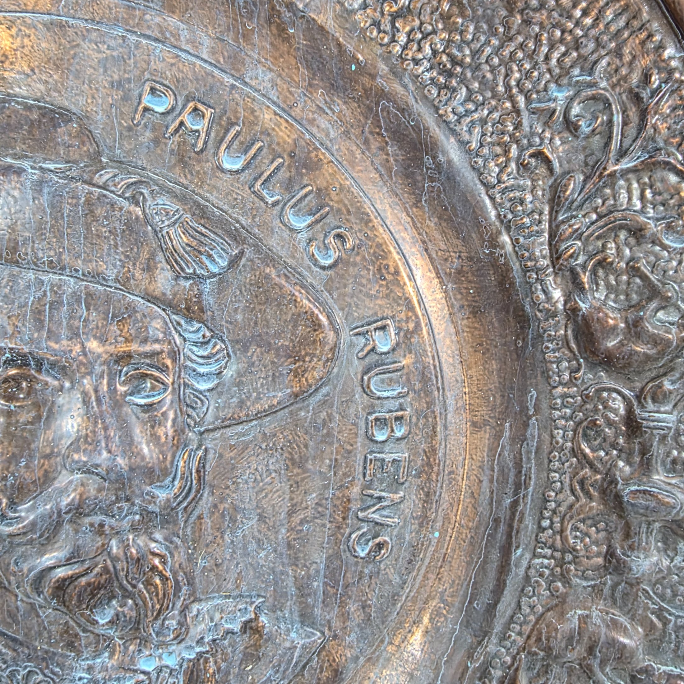 A collection of four vintage embossed metal wall plaques, comprising a large copper-toned plaque featuring a portrait of Peter Paul Rubens, two brass-toned plaques depicting fox hunting and horse-drawn carriage scenes, and a smaller copper-toned plaque with a tavern scene. - View 4