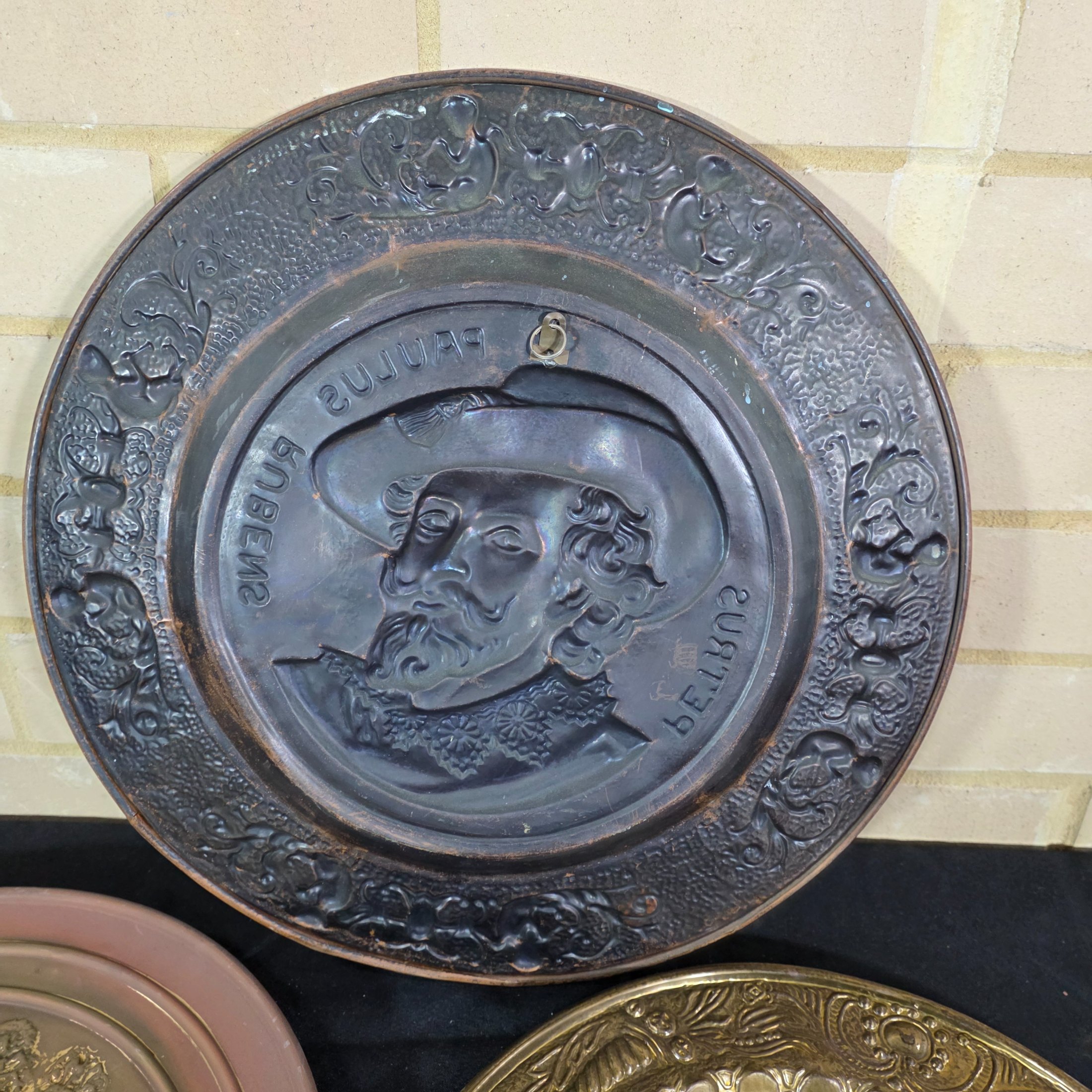 A collection of four vintage embossed metal wall plaques, comprising a large copper-toned plaque featuring a portrait of Peter Paul Rubens, two brass-toned plaques depicting fox hunting and horse-drawn carriage scenes, and a smaller copper-toned plaque with a tavern scene. - View 6