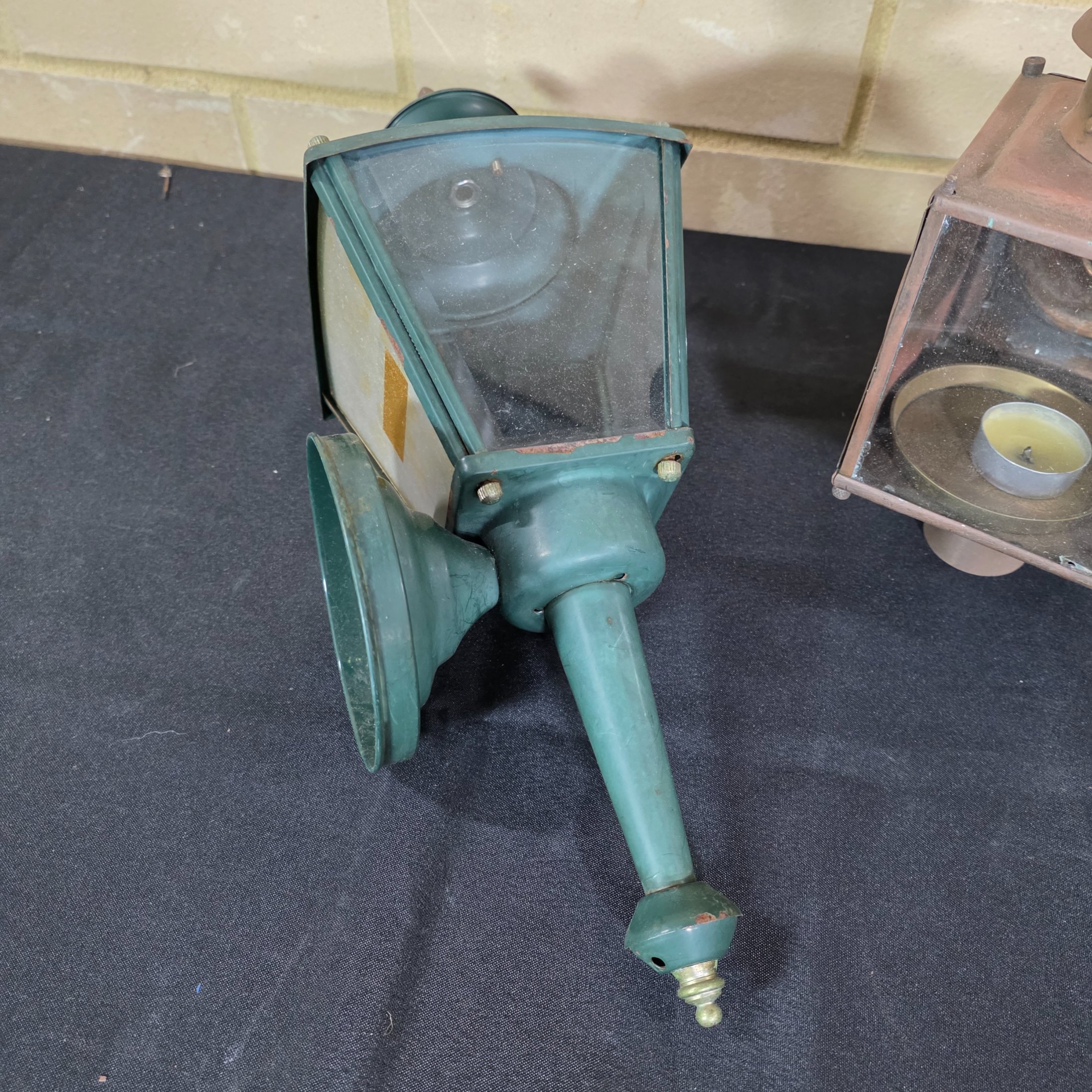A diverse lot of three vintage outdoor lanterns, comprising a green wall-mounted electric light, an older copper-toned candle lantern, and a black painted Kempthorne electric wall sconce with amber glass. - View 2