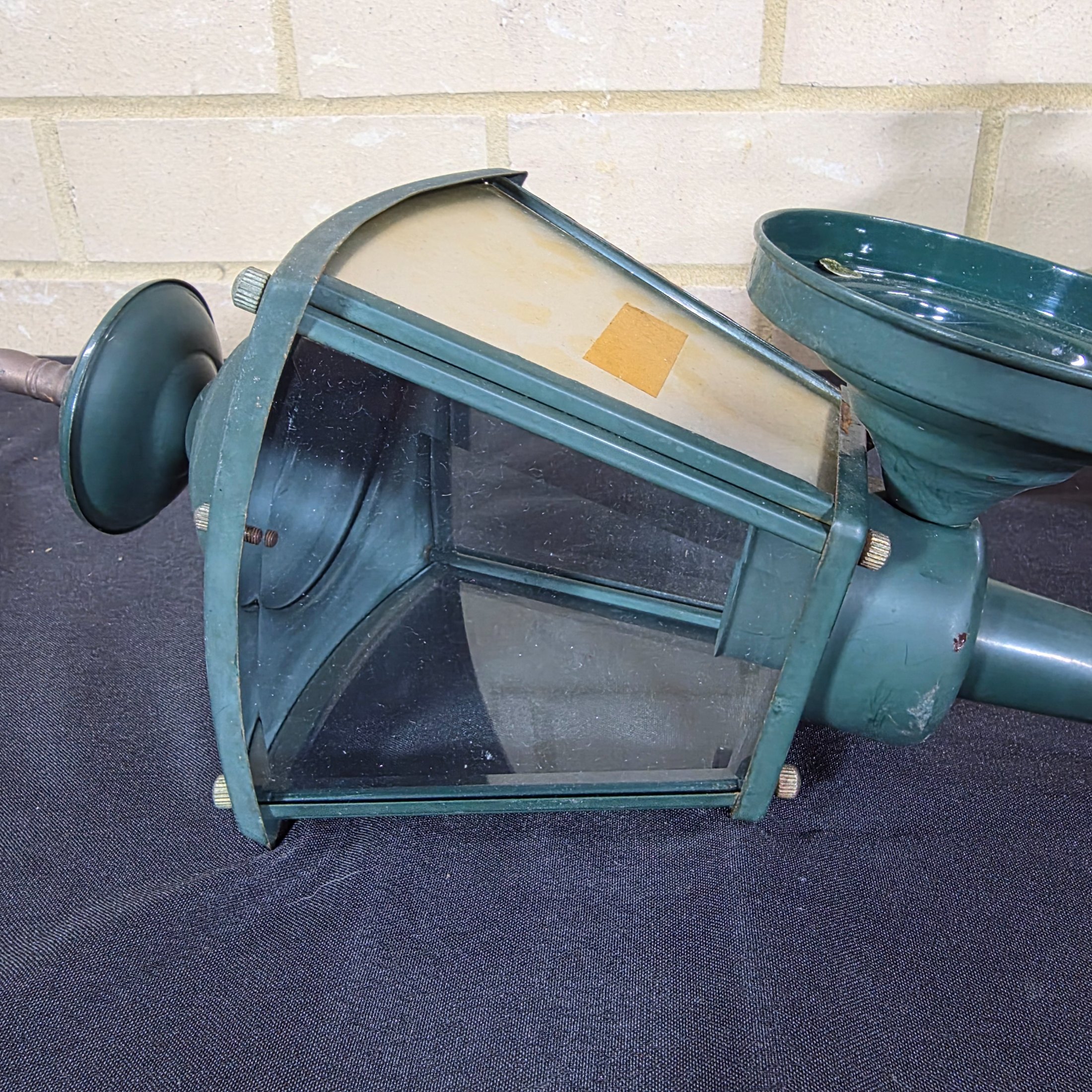 A diverse lot of three vintage outdoor lanterns, comprising a green wall-mounted electric light, an older copper-toned candle lantern, and a black painted Kempthorne electric wall sconce with amber glass. - View 3