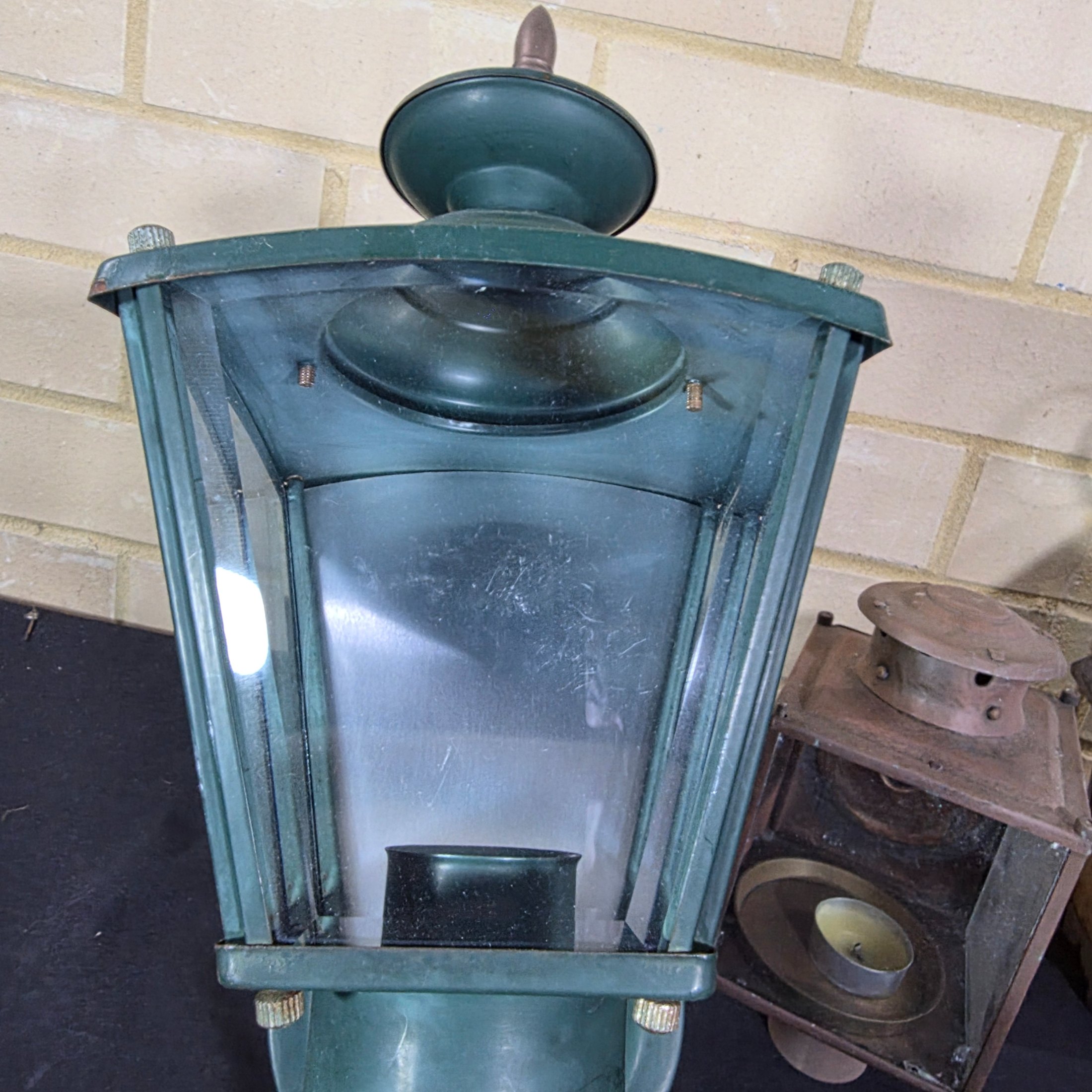 A diverse lot of three vintage outdoor lanterns, comprising a green wall-mounted electric light, an older copper-toned candle lantern, and a black painted Kempthorne electric wall sconce with amber glass. - View 6