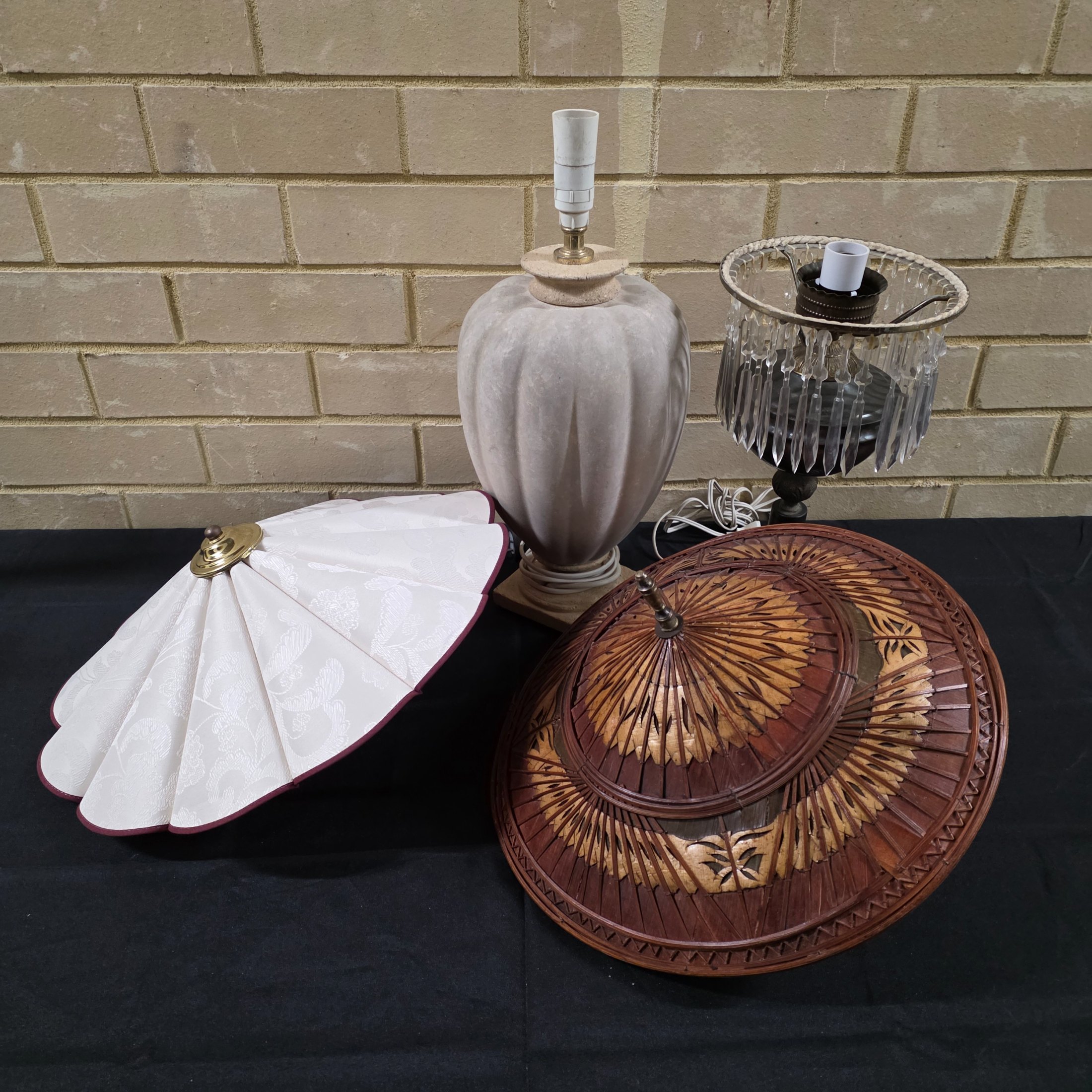 A lot consisting of two vintage lamp bases – one cream-grey fluted ceramic and one bronze-toned with hanging clear crystals – alongside a white pleated fabric lampshade and an intricately carved wooden lampshade.