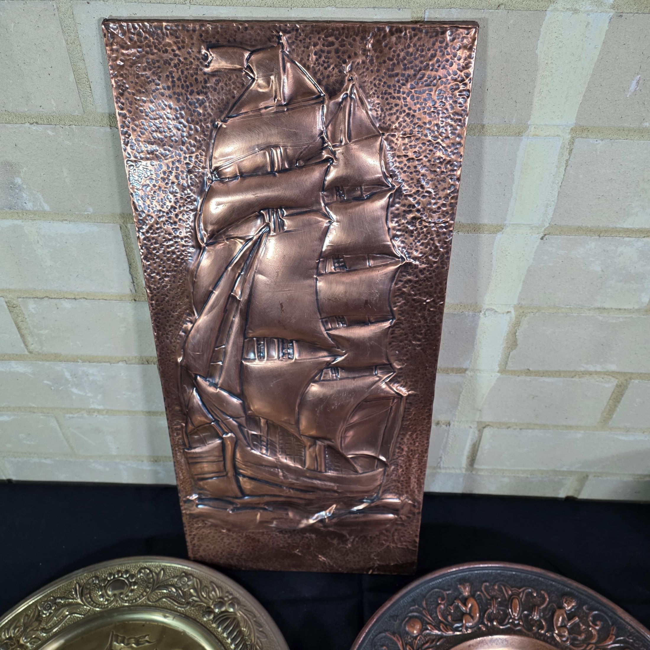A collection of three vintage embossed metal decorative items, including a rectangular copper wall hanging and two round plates, all depicting sailing ships. - View 2