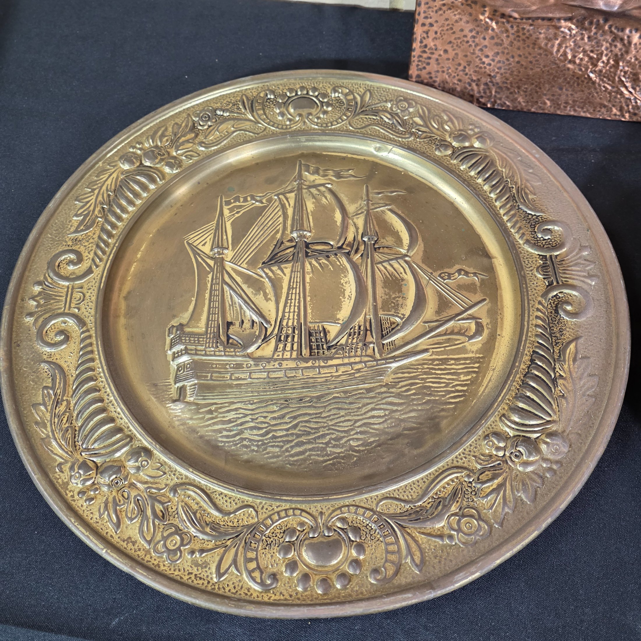 A collection of three vintage embossed metal decorative items, including a rectangular copper wall hanging and two round plates, all depicting sailing ships. - View 3